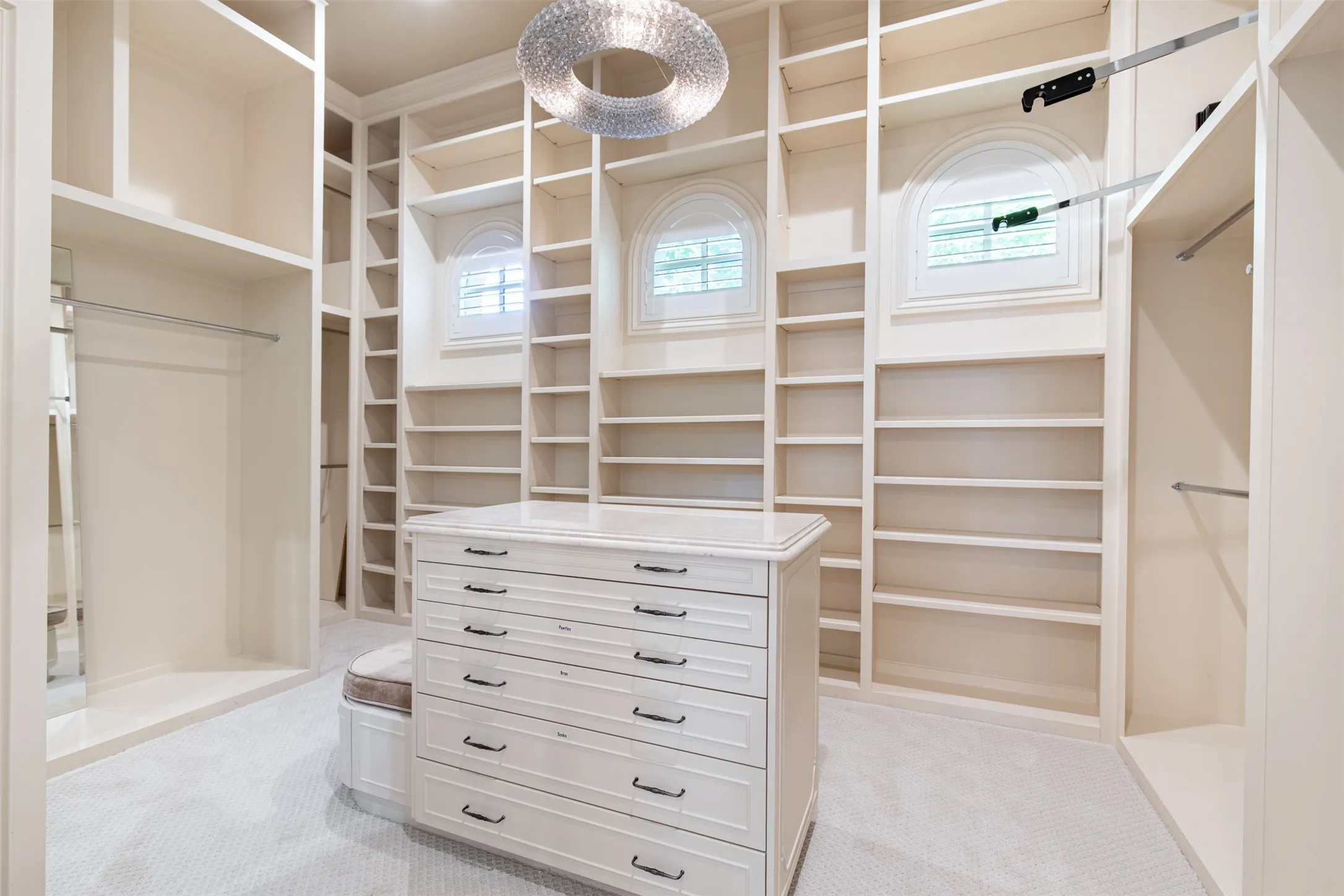 Custom closet featuring extensive built-in shelving, a central dresser island with multiple drawers, and two arched windows with plantation shutters. Dual closets in the primary suite.