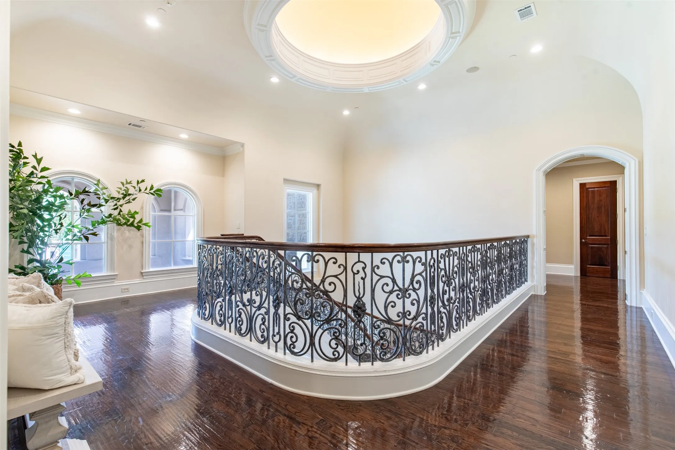 Upper-level landing featuring a large ornate wrought iron and wood-finish railing, recessed lighting, and a domed ceiling detail with ambient illumination