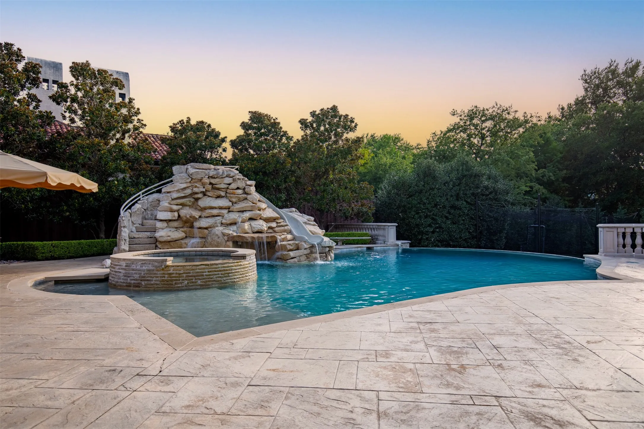 Spacious infinity pool with elevated spa, tanning ledge area featuring a custom rock waterfall, and an irregular-shaped pool