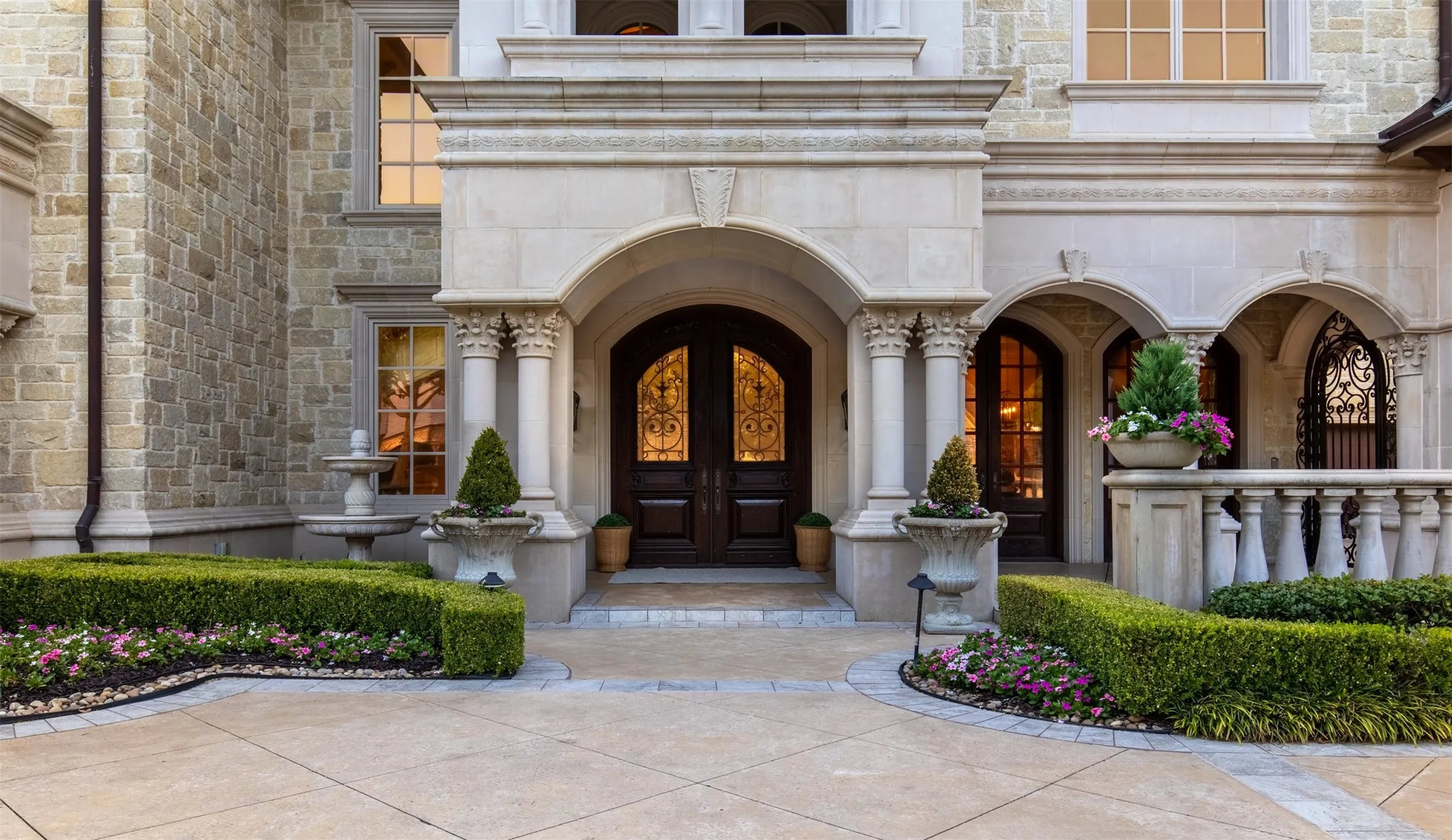Elegant stone entryway featuring double wooden glass and wood doors, decorative ironwork, and stately columns. Gated entry to the motor court.