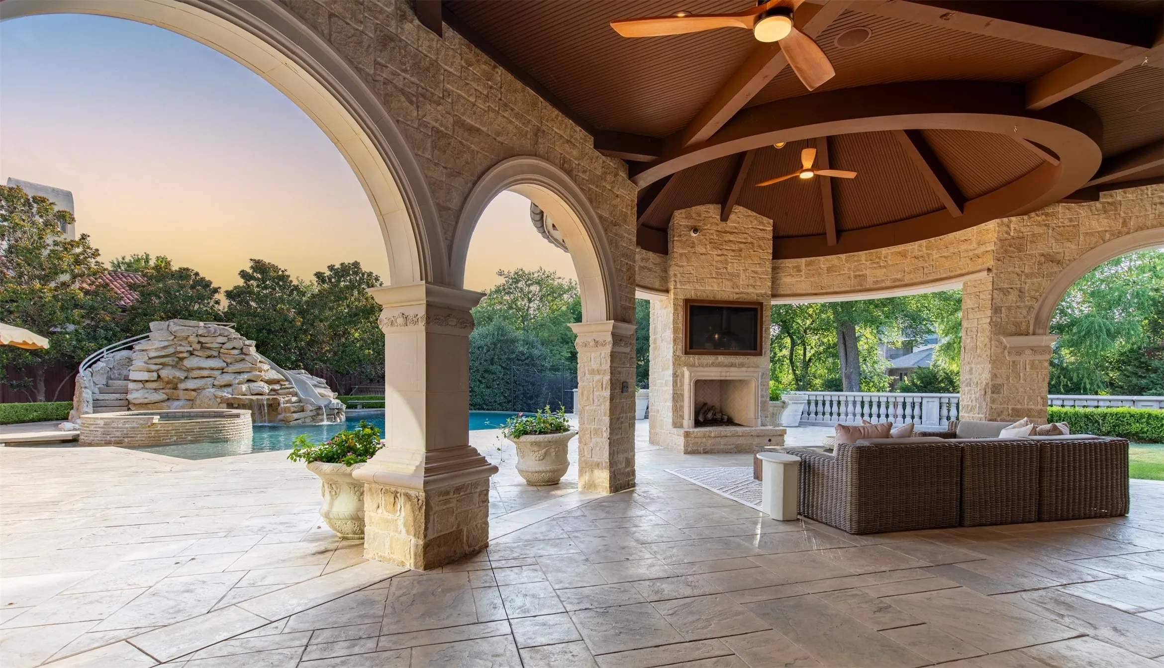 Expansive outdoor covered lanai featuring stone arches, a built-in fireplace, and a wood-finish ceiling with integrated fans and full outdoor kitchen