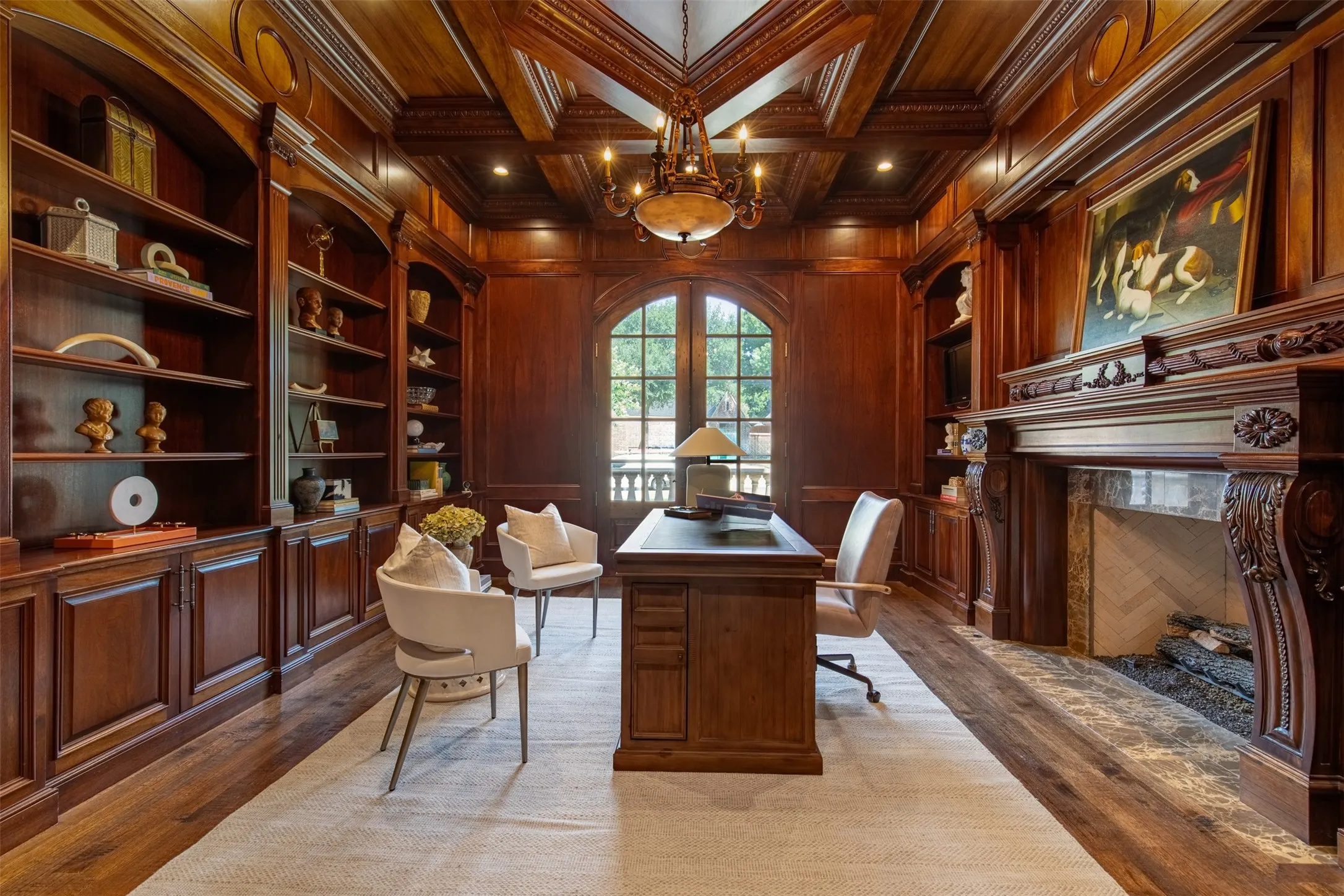 Rich wood paneling throughout executive office with built-in shelving, ornate fireplace with carved mantel with marble fireplace, nail down hardwood floors and arched French doors to front patio