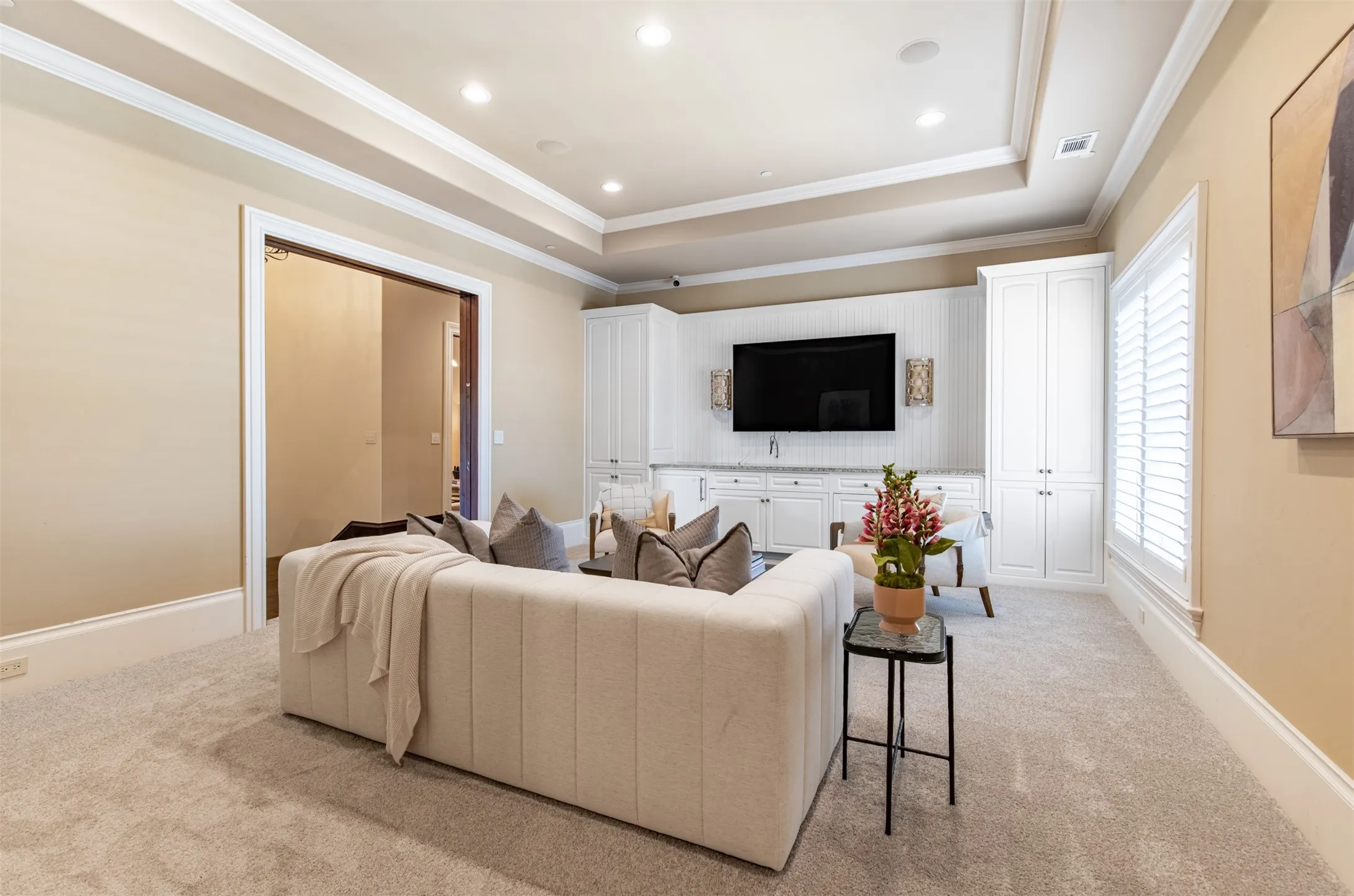 Spacious upstairs living room featuring a tray ceiling with recessed lighting, custom built-in cabinetry, with a tiled backsplash, and plantation shutters