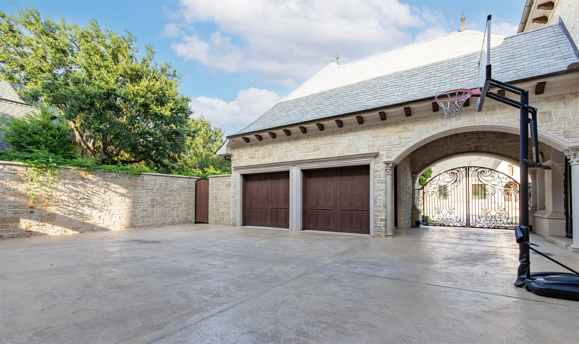 Gated motor court with stone privacy fence exterior featuring five-car garage with wood-finish doors, an arched entryway, and a slate tile roof