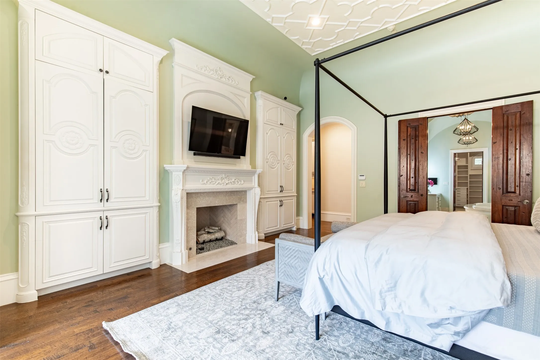 Elegant interior showcasing a decorative gas fireplace with a mounted television, flanked by custom white cabinetry and ensuite bathroom.