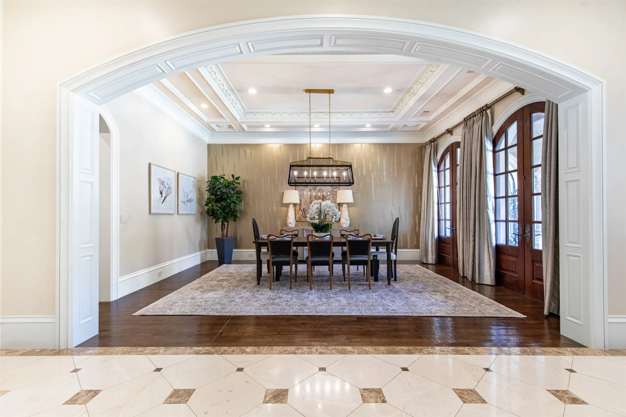 Elegant dining room featuring a coffered ceiling, a contemporary chandelier, two sets of arched French doors, nail down hardwood floors. Located off the front of the home with Butler Pantry pass through to the Kitchen