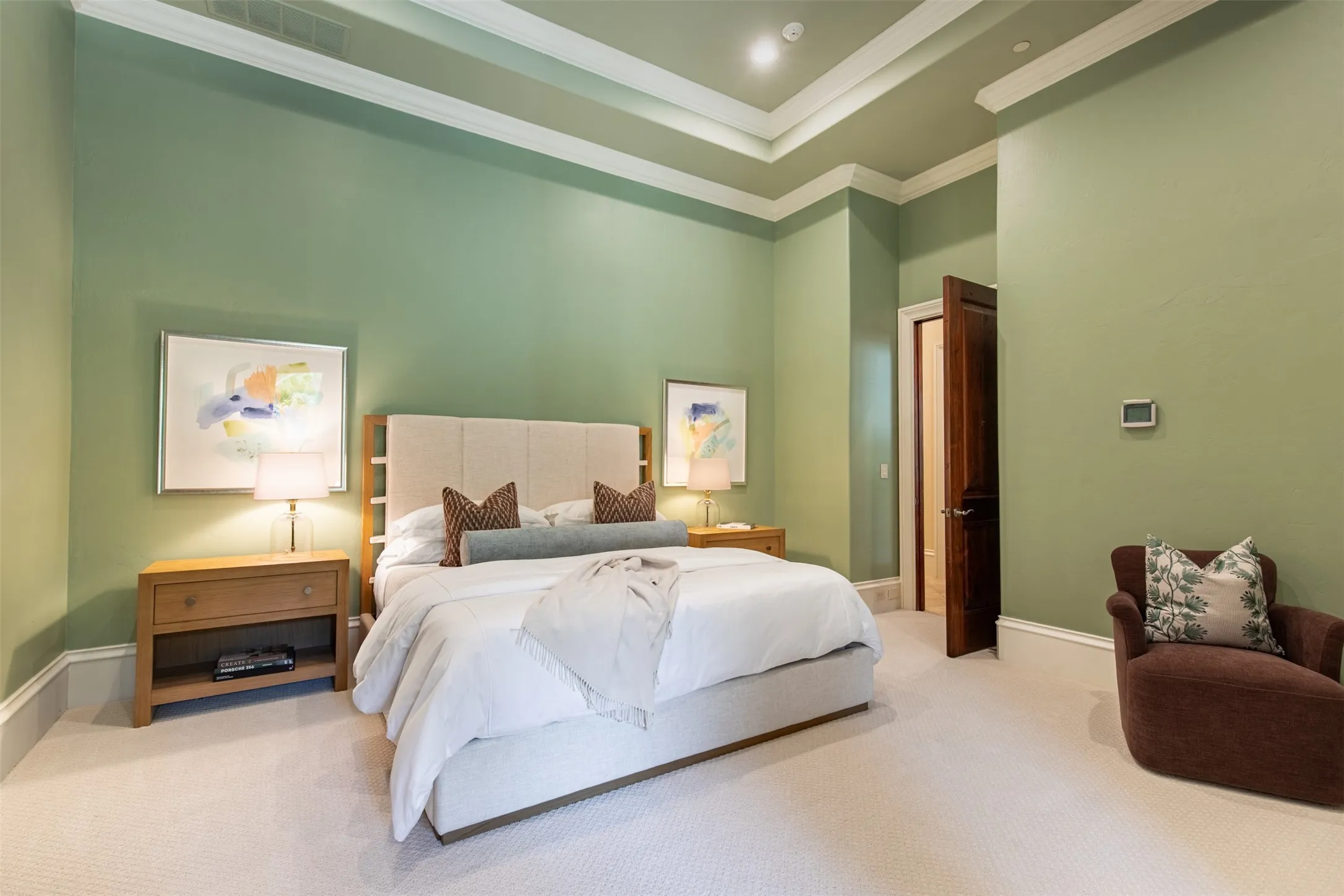 Spacious downstairs guest bedroom featuring light green walls, a tray ceiling with crown molding, and light-colored carpeting, ensuite bathroom and double doors to exterior