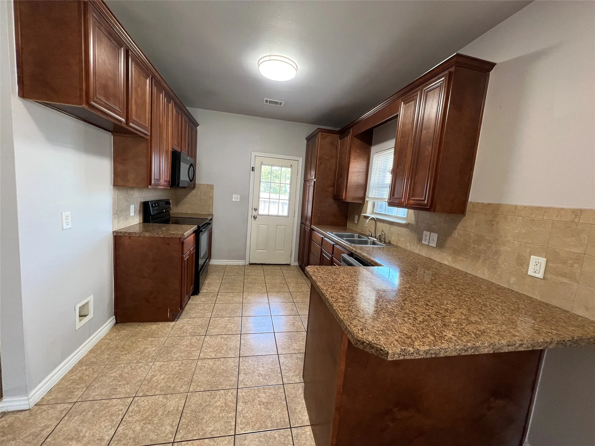Kitchen featuring wood-finish cabinetry, granite-style countertops, tiled flooring, stainless steel sink, and black appliances