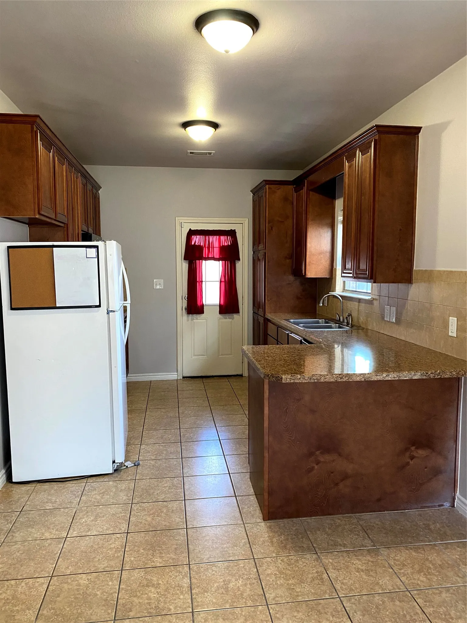 Kitchen featuring wood-finish cabinetry, granite-style countertops, and a tile backsplash