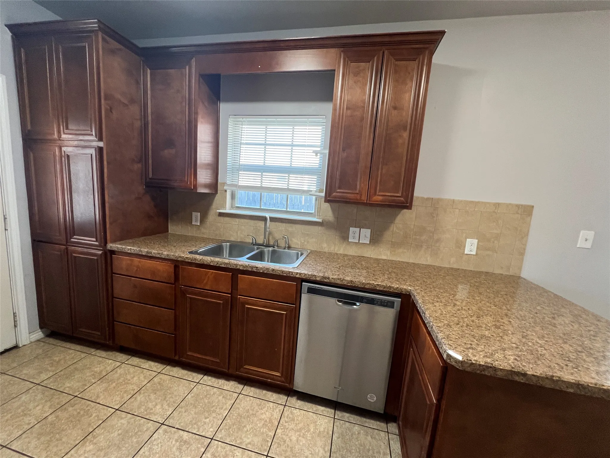 Wood cabinetry, granite-finish countertops, stainless steel dishwasher, tile flooring, and a tile backsplash
