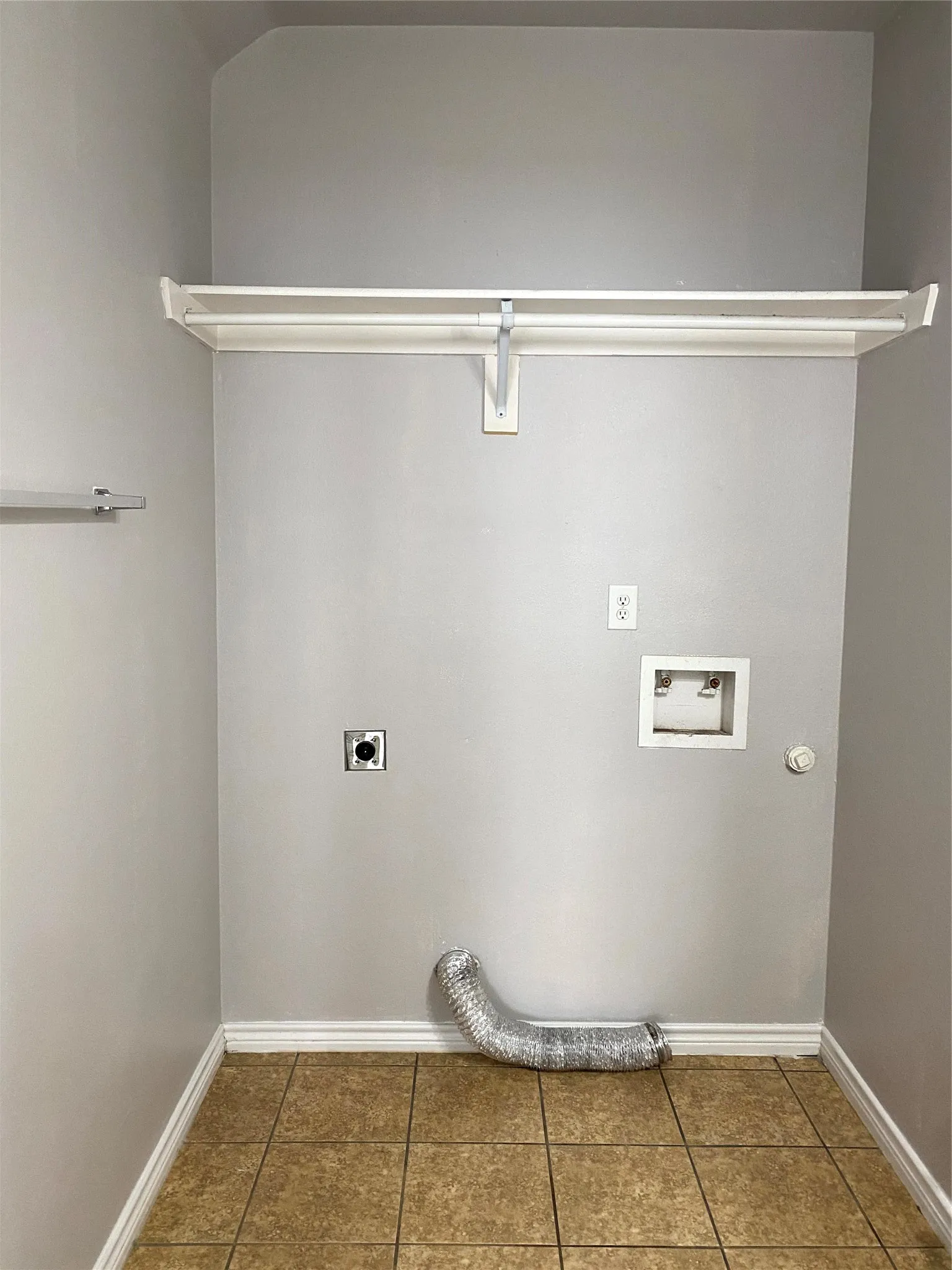 Dedicated laundry space featuring neutral-toned walls, a white storage shelf, durable tiled flooring, and essential hookups for appliances