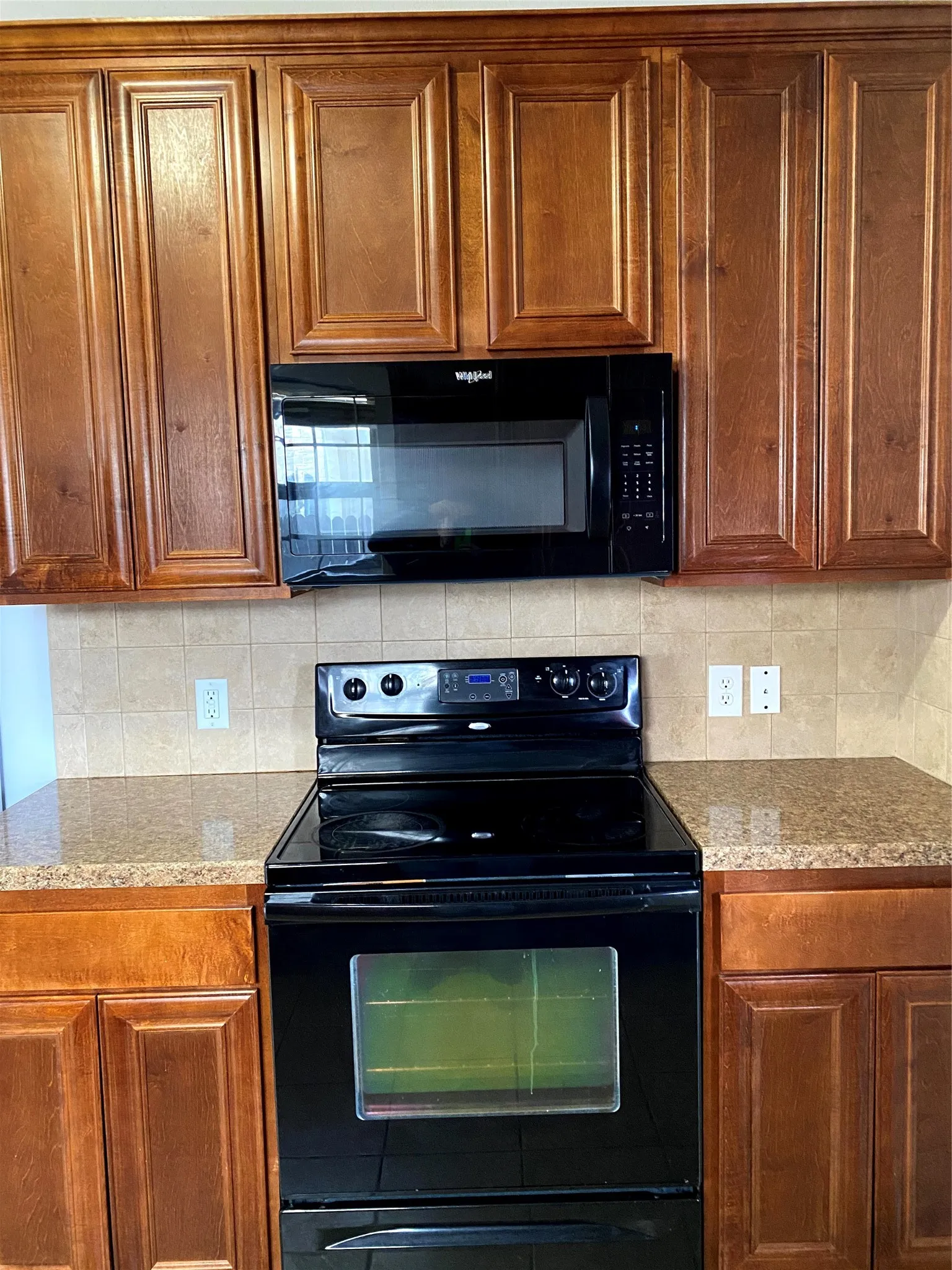 Kitchen featuring rich wood cabinetry, black built-in microwave, black electric range, and granite-style countertops with a tiled backsplash