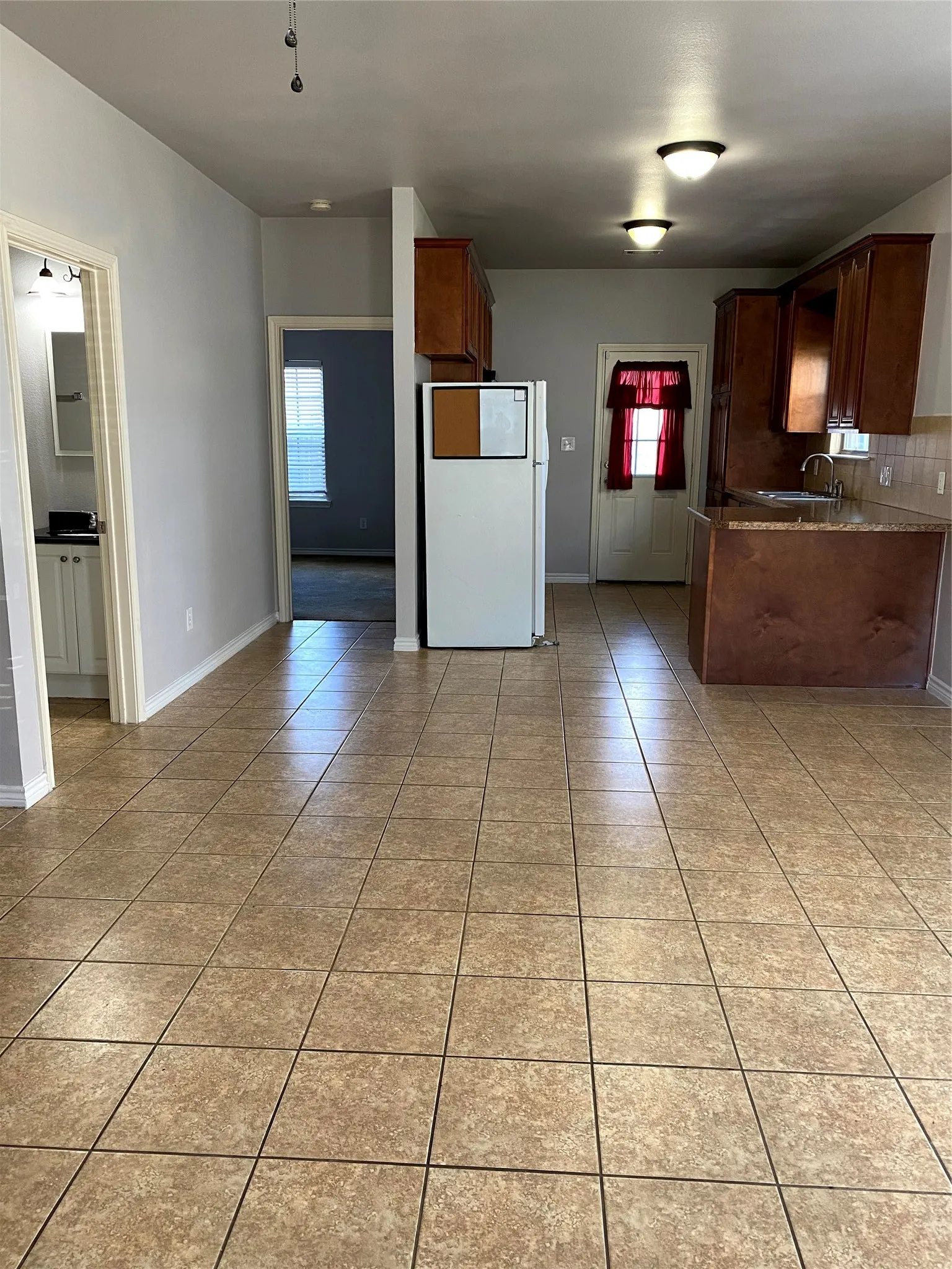 Kitchen and living area featuring neutral tile flooring, warm wood cabinetry, a granite-finish countertop, and recessed ceiling lighting