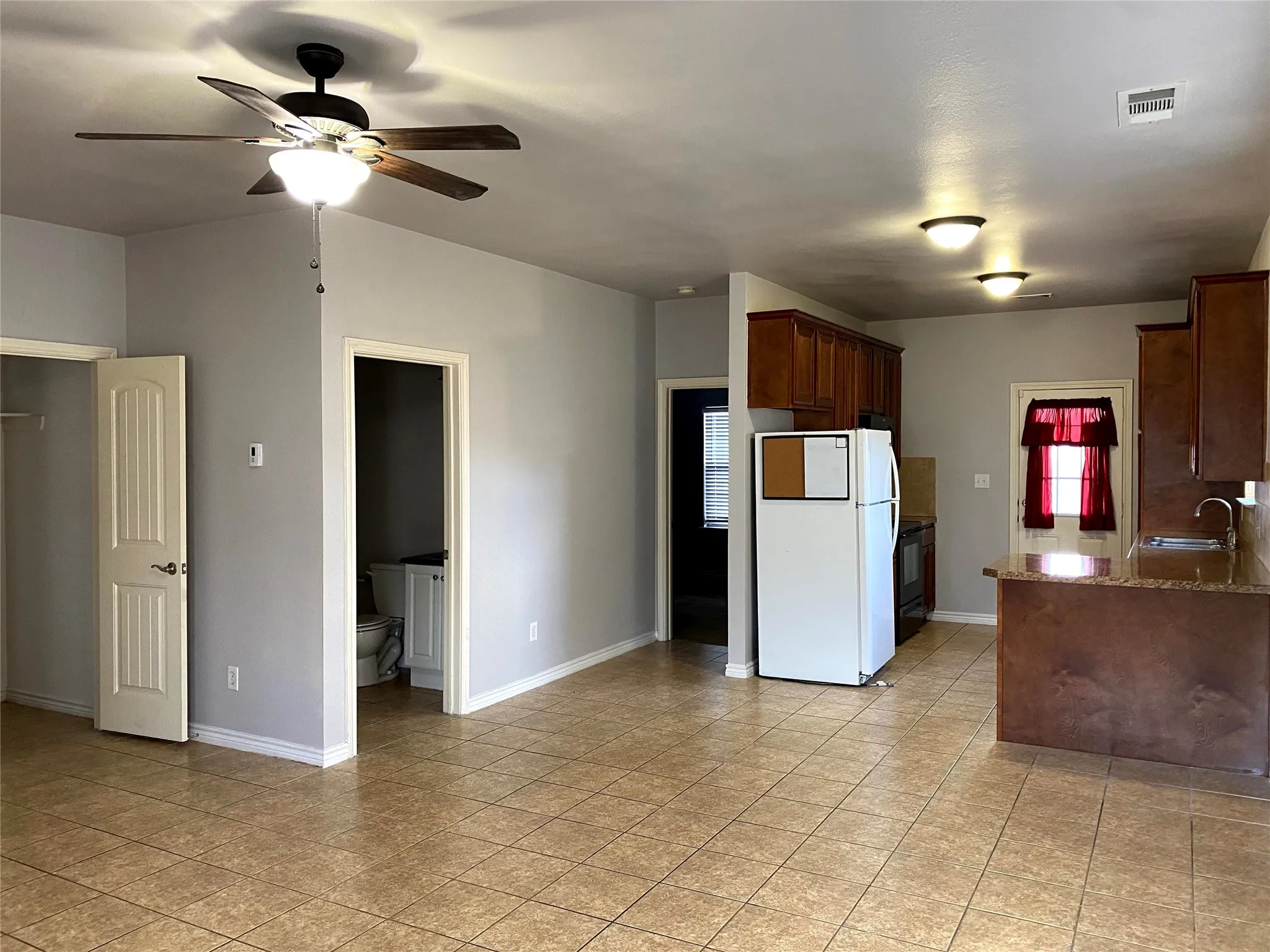 Open concept living area featuring ceramic tile flooring, a kitchen with wood-finish cabinetry, and a ceiling fan with integrated lighting