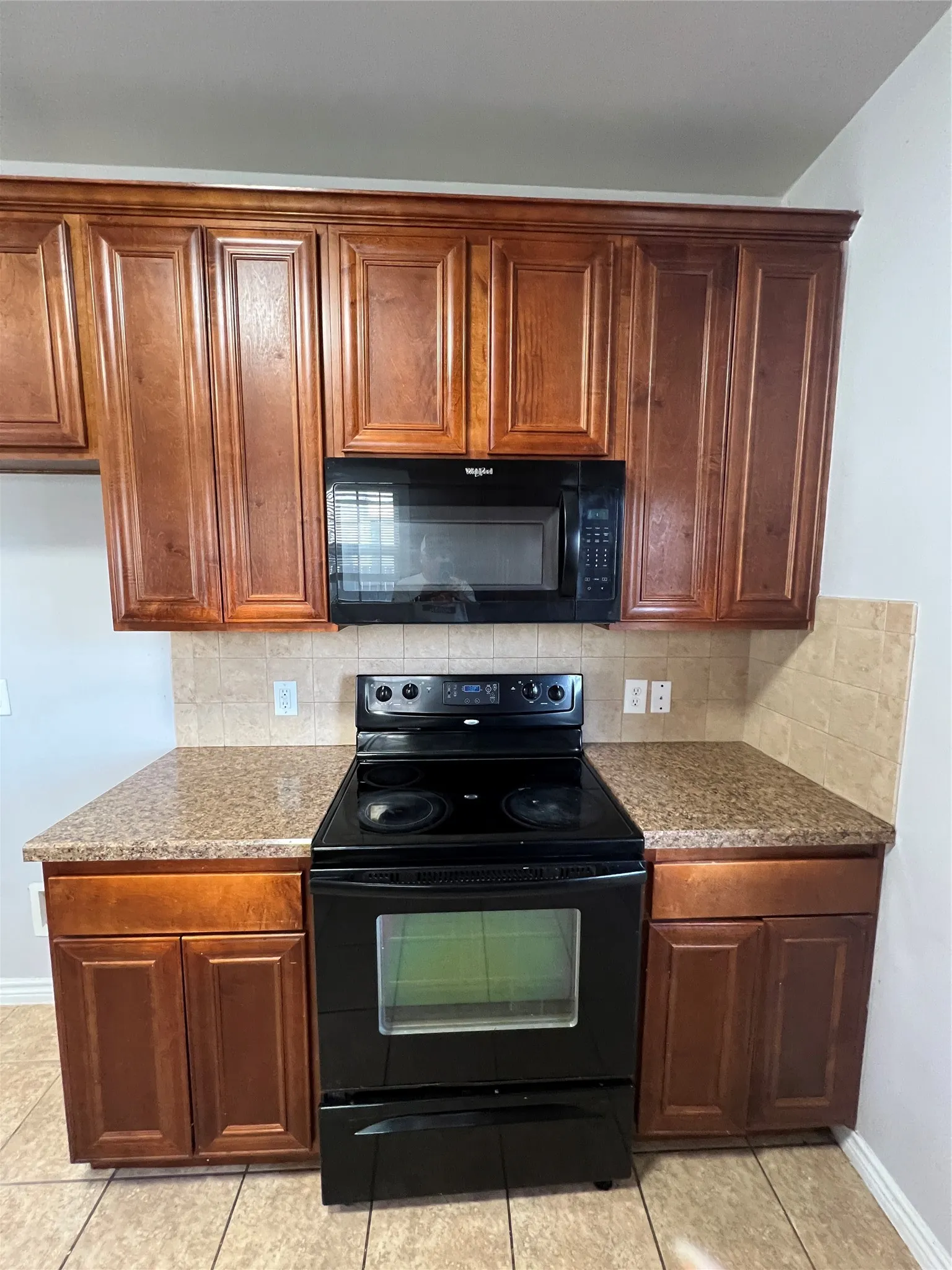 Compact kitchen featuring rich wood cabinetry with raised-panel doors, granite-style countertops, and black electric range with viewing window