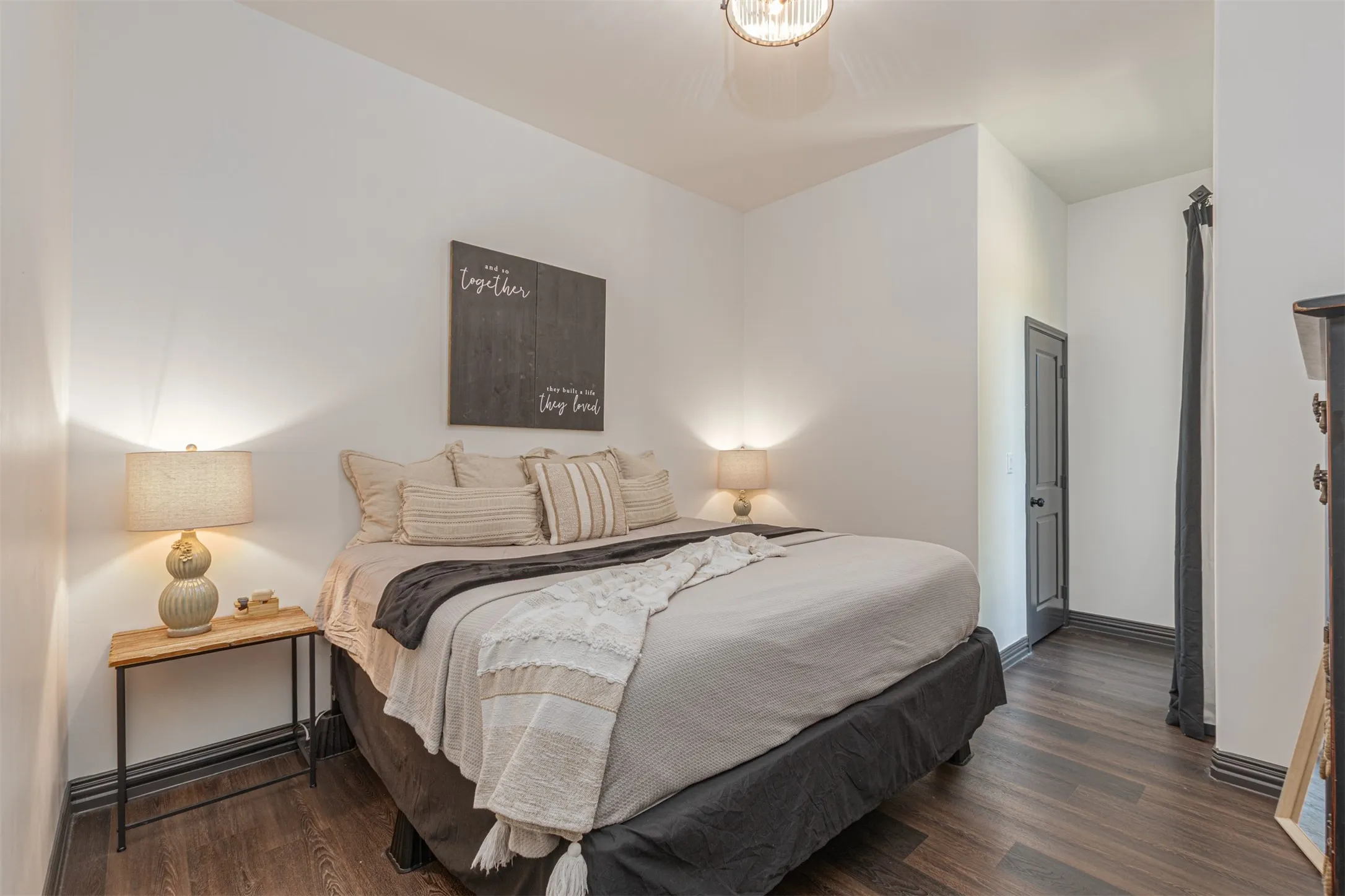 Interior room featuring wood-finish flooring, white walls, dark trim, and a dark paneled door