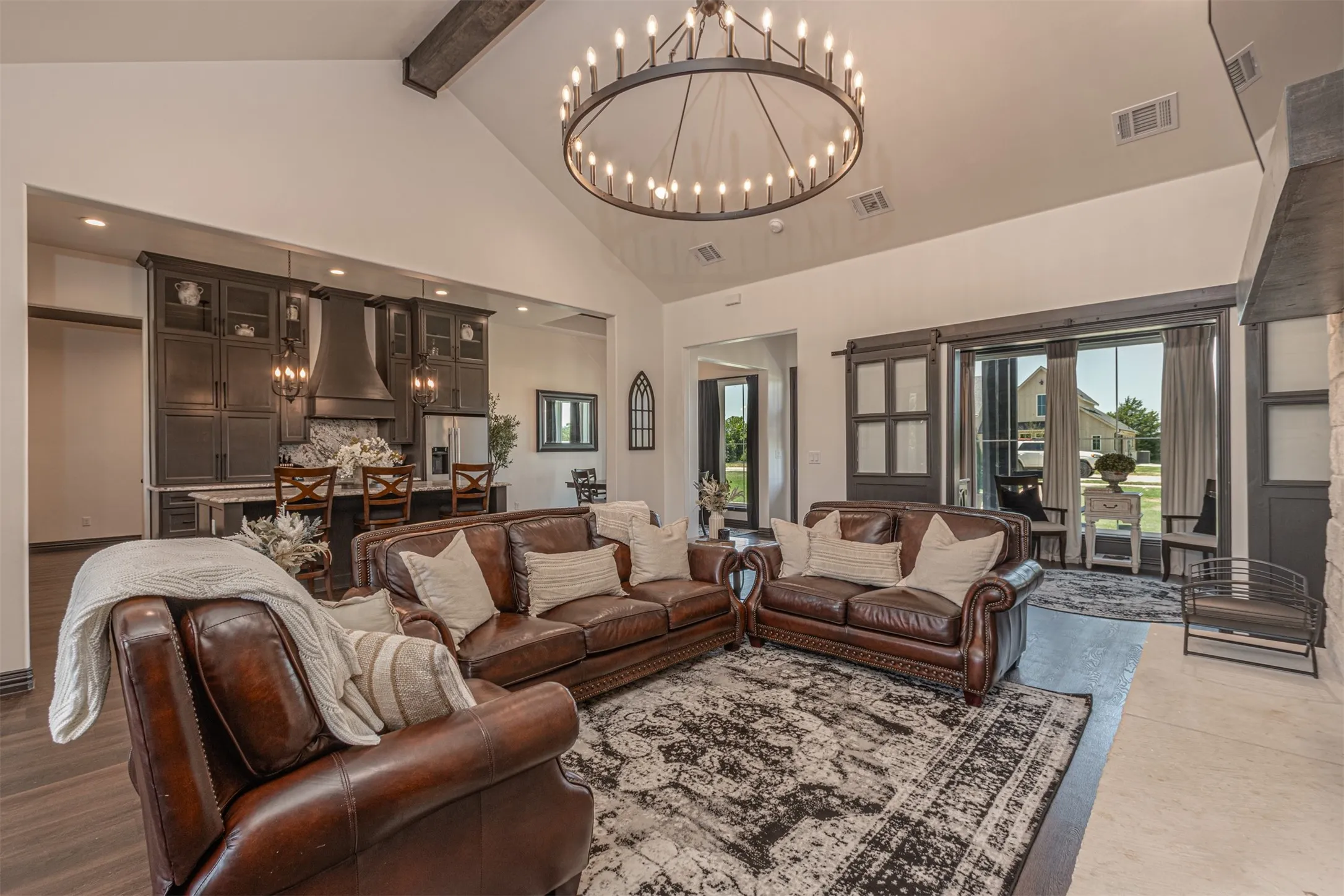 Spacious living area featuring a vaulted ceiling with exposed wood-finish beam, a large circular chandelier, and light-tone tile flooring