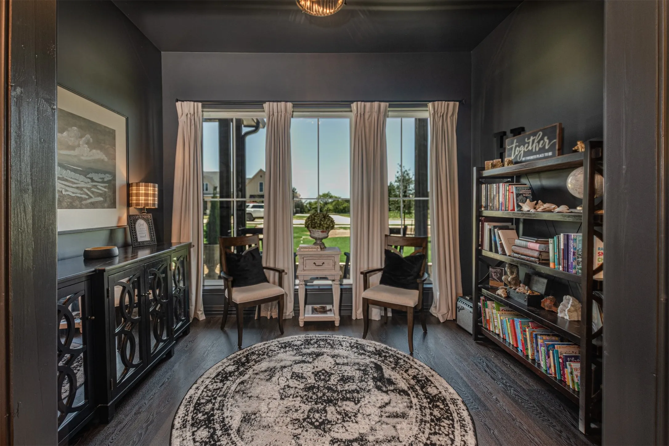 Room featuring dark-toned walls, wood-finish flooring, a built-in shelving unit, and a prominent window array