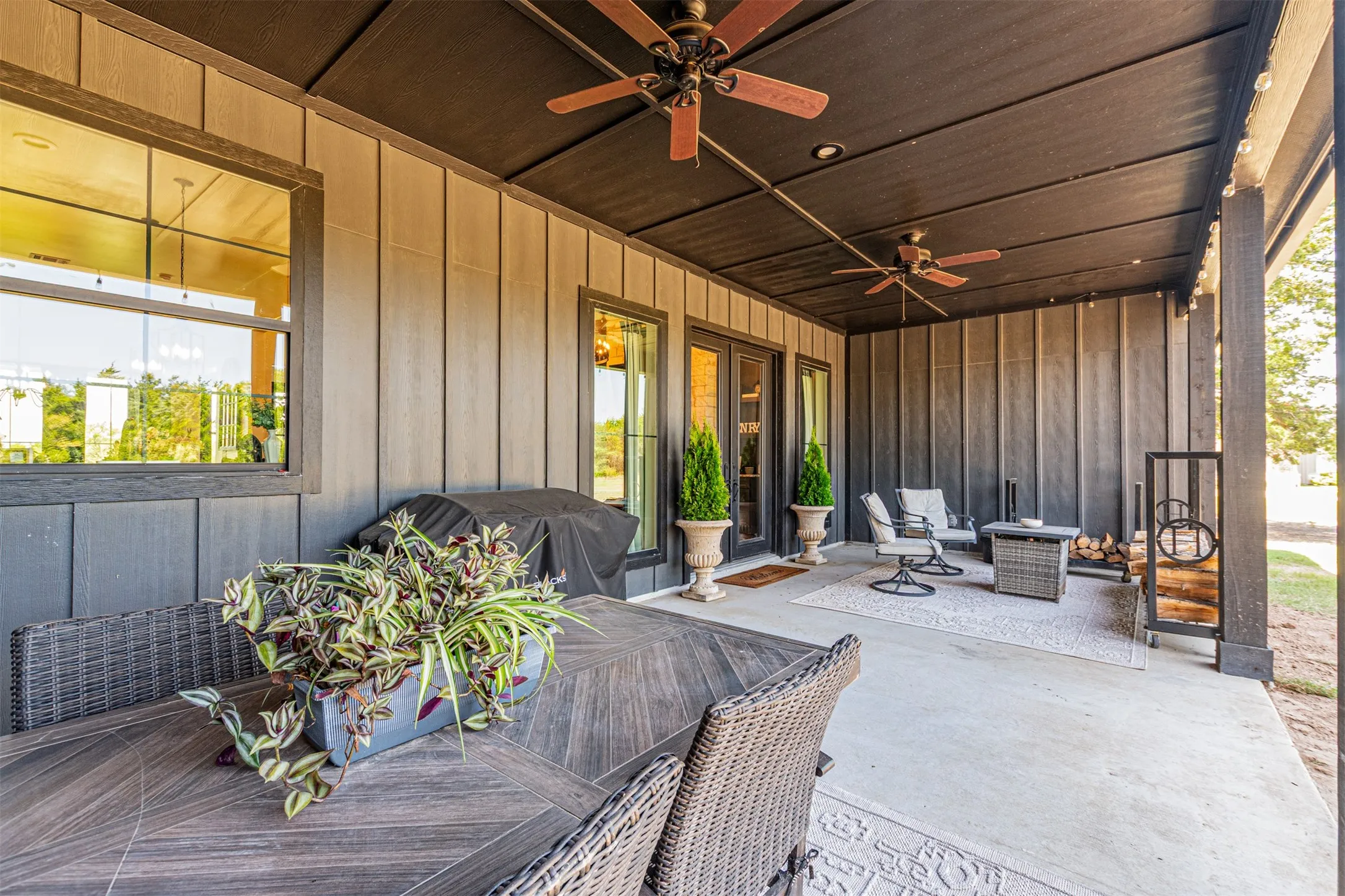 Covered patio featuring a dark wood-finish ceiling, board and batten siding, two ceiling fans, and a concrete floor