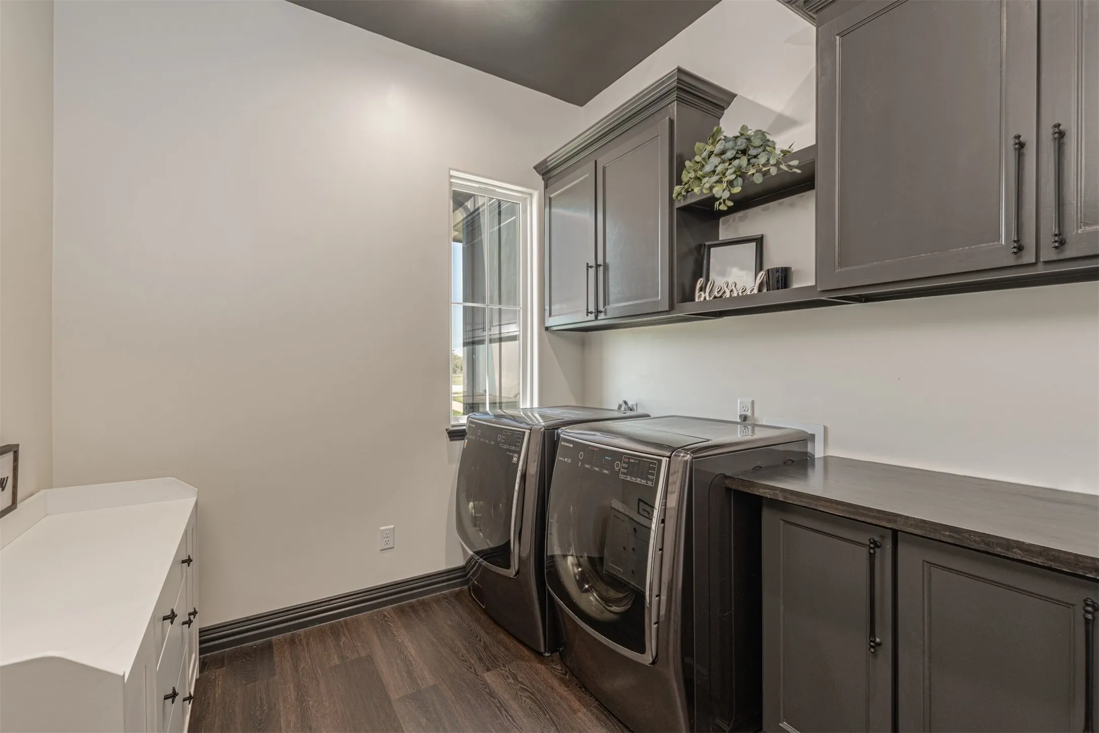 Dedicated laundry space featuring dark wood-finish flooring, a white countertop with built-in drawers, and extensive gray cabinetry with dark hardware