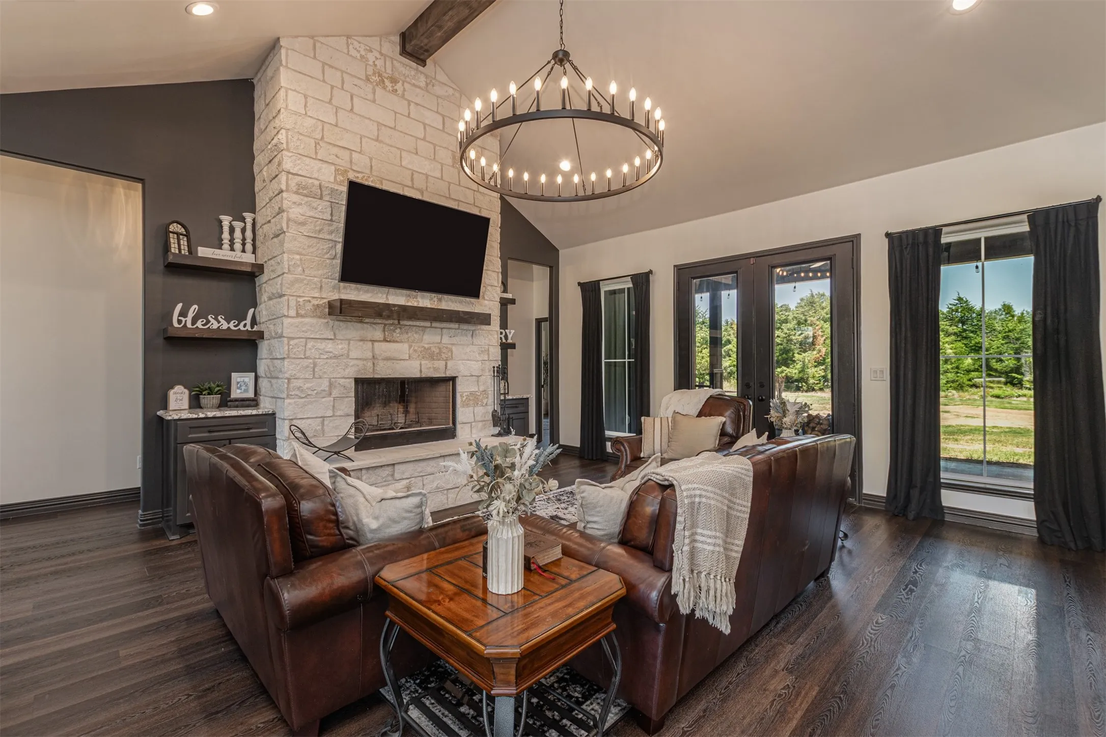 Living area featuring a stone fireplace with a wood mantle, vaulted ceiling with exposed wood beam, and a large circular chandelier