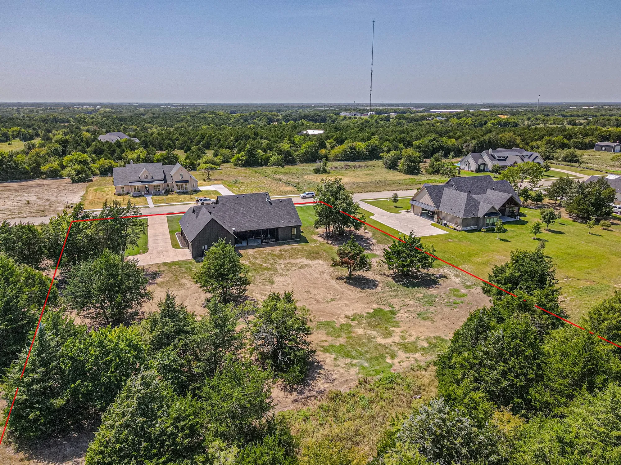 Expansive property featuring a dark-toned residential structure with a covered front porch and a paved driveway