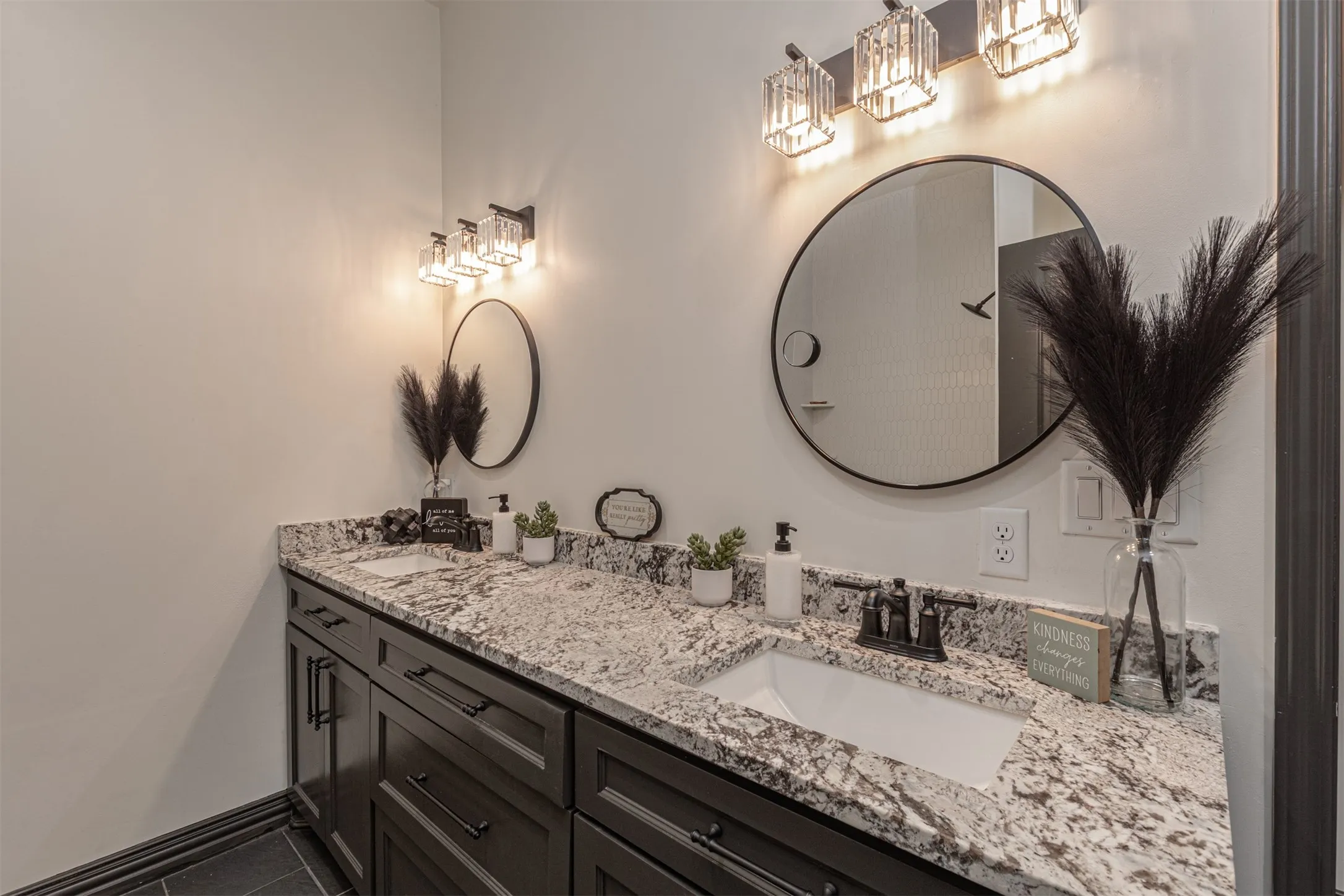 Double vanity featuring dark wood cabinetry, light granite countertops, undermount sinks, and matte black fixtures