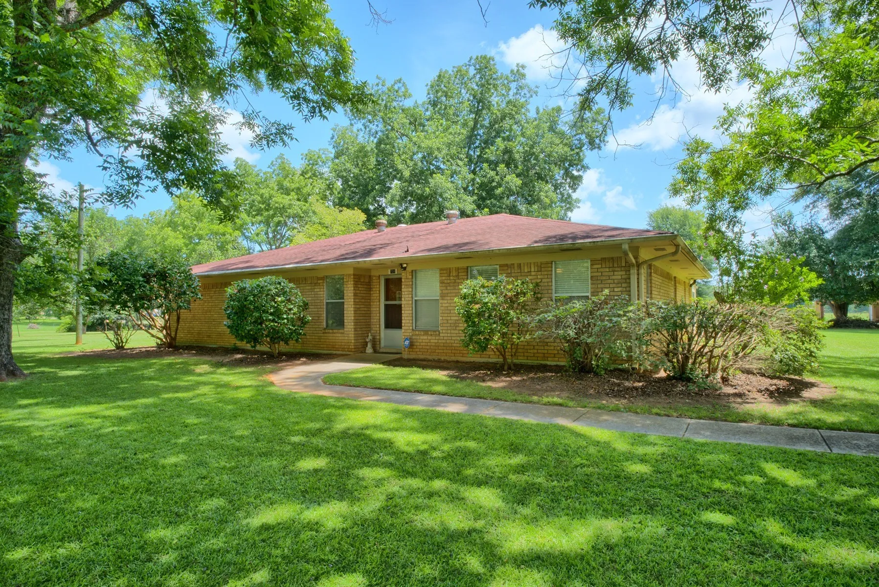 Brick exterior residence featuring a front yard with mature trees, a curved concrete walkway,