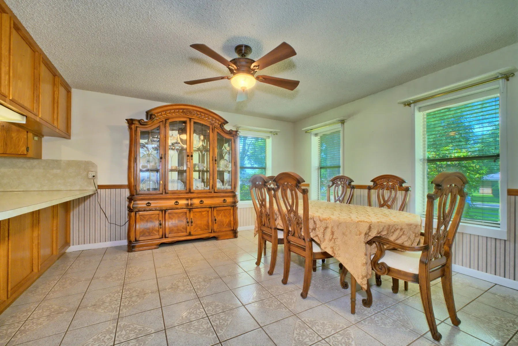 Open-concept dining area featuring light-toned tile flooring, light wood cabinetry, and a ceiling fan with integrated lighting