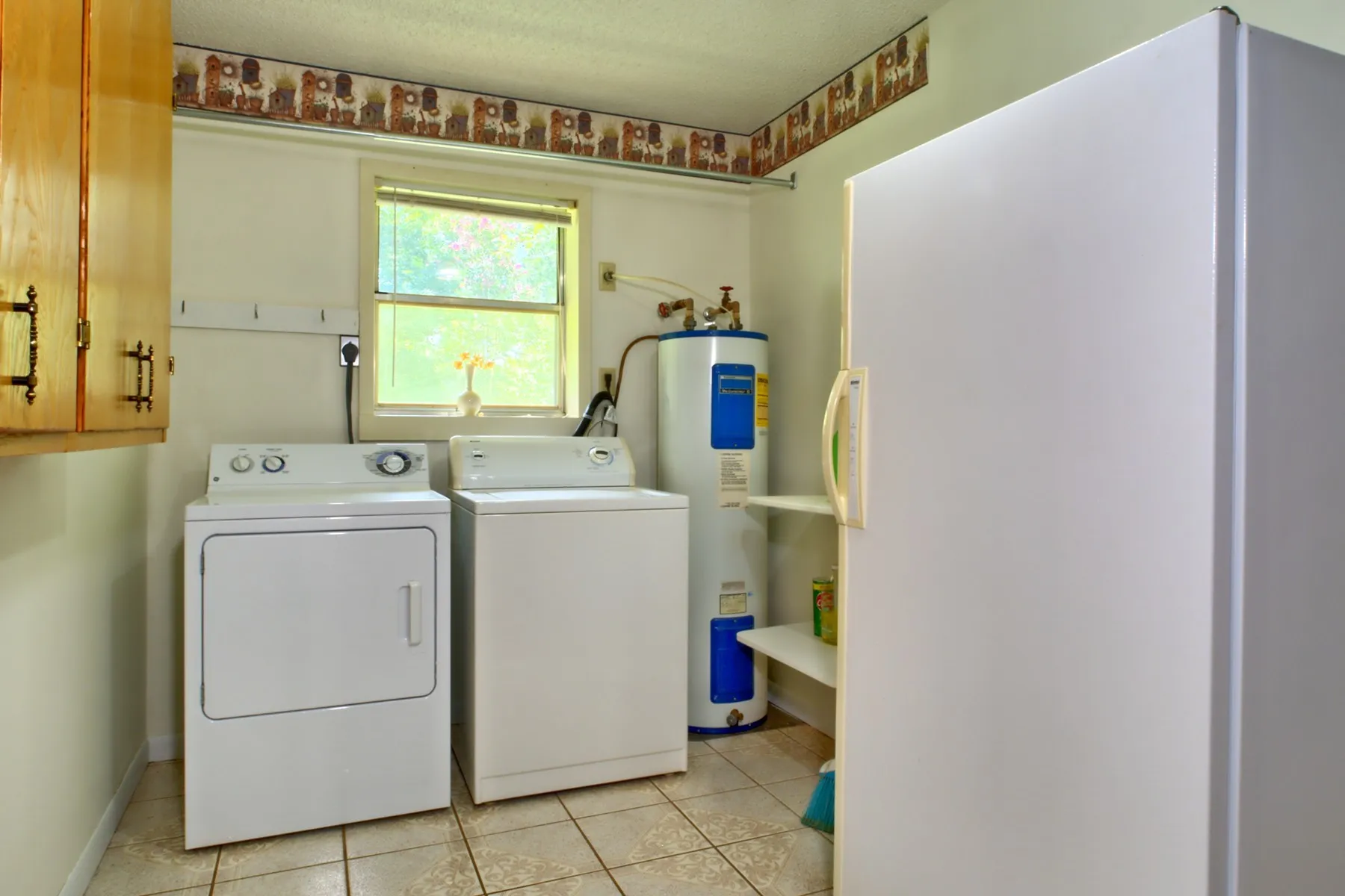 Utility room featuring a window, tile flooring, wall-mounted cabinetry, and a hot water heater