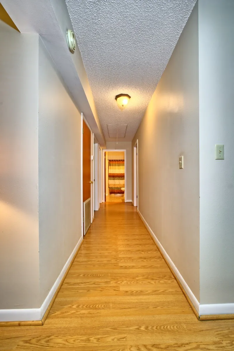 Hallway featuring wood-finish flooring, light neutral wall paint, and white baseboards - leads to 3 bedrooms and 2 baths