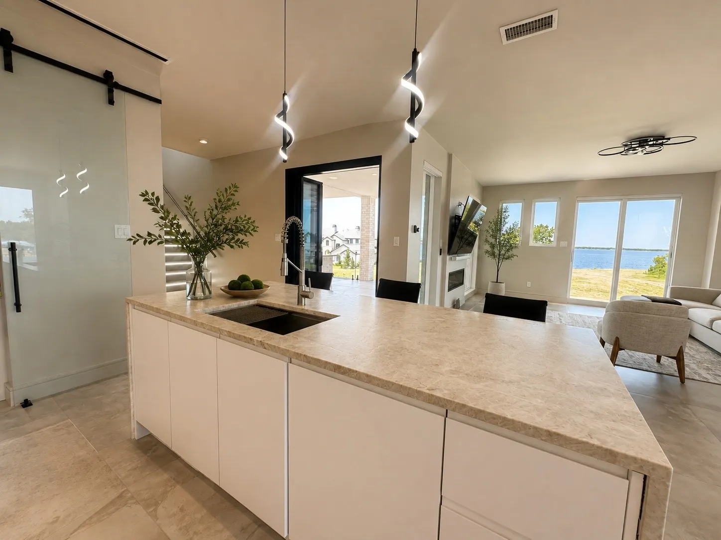 Expansive Taj Mahal quartz stone island anchors the open-concept kitchen, showcasing contemporary lighting, sleek cabinetry, and beautiful lake views from the adjoining living area.