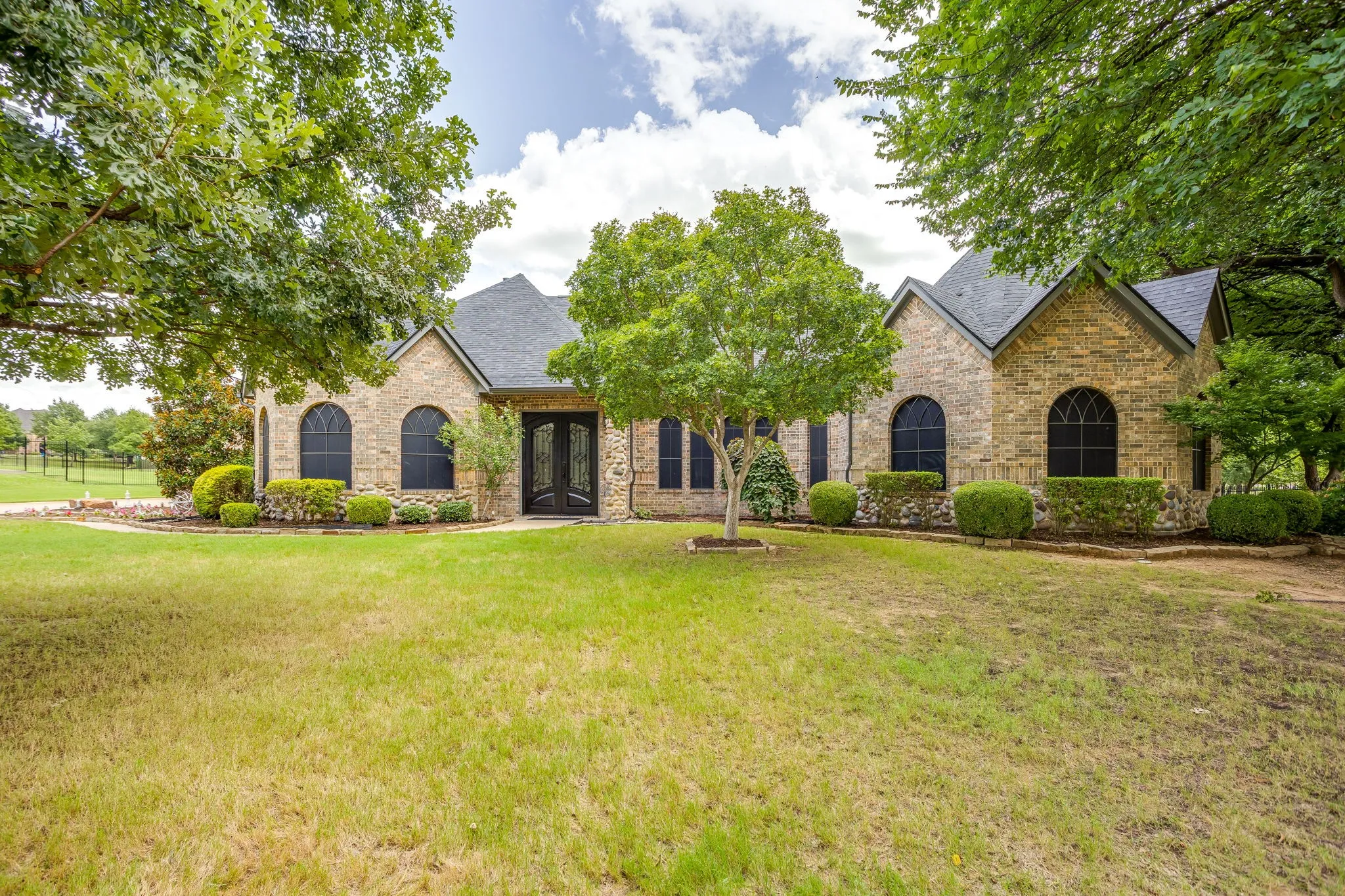 Stone facade residence featuring a dark shingled roof and symmetrical arched windows