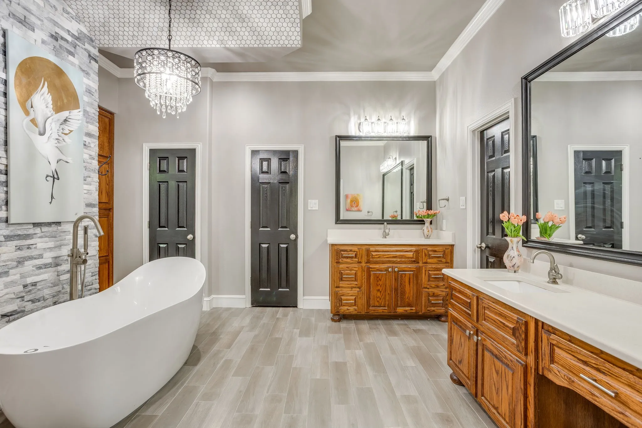 Freestanding soaking tub with a floor-mounted faucet, complemented by a stone accent wall and a crystal chandelier
