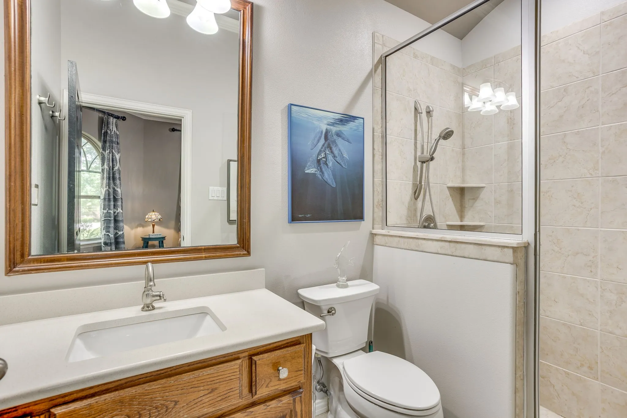 Bathroom featuring a wood-finish vanity with an integrated sink, a large framed mirror, and a tiled shower enclosure with a glass panel