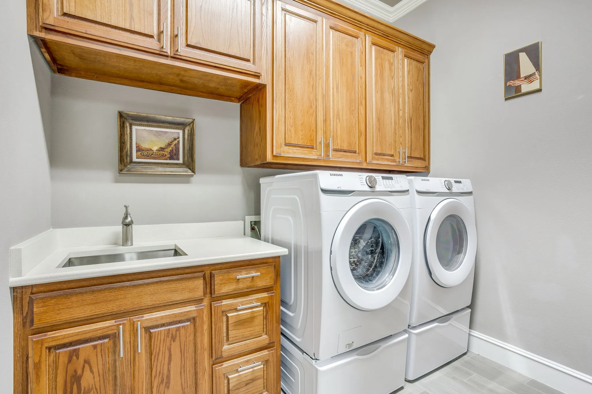 Laundry area featuring custom wood cabinetry with crown molding, a built-in utility sink with stainless steel faucet, and solid surface countertops