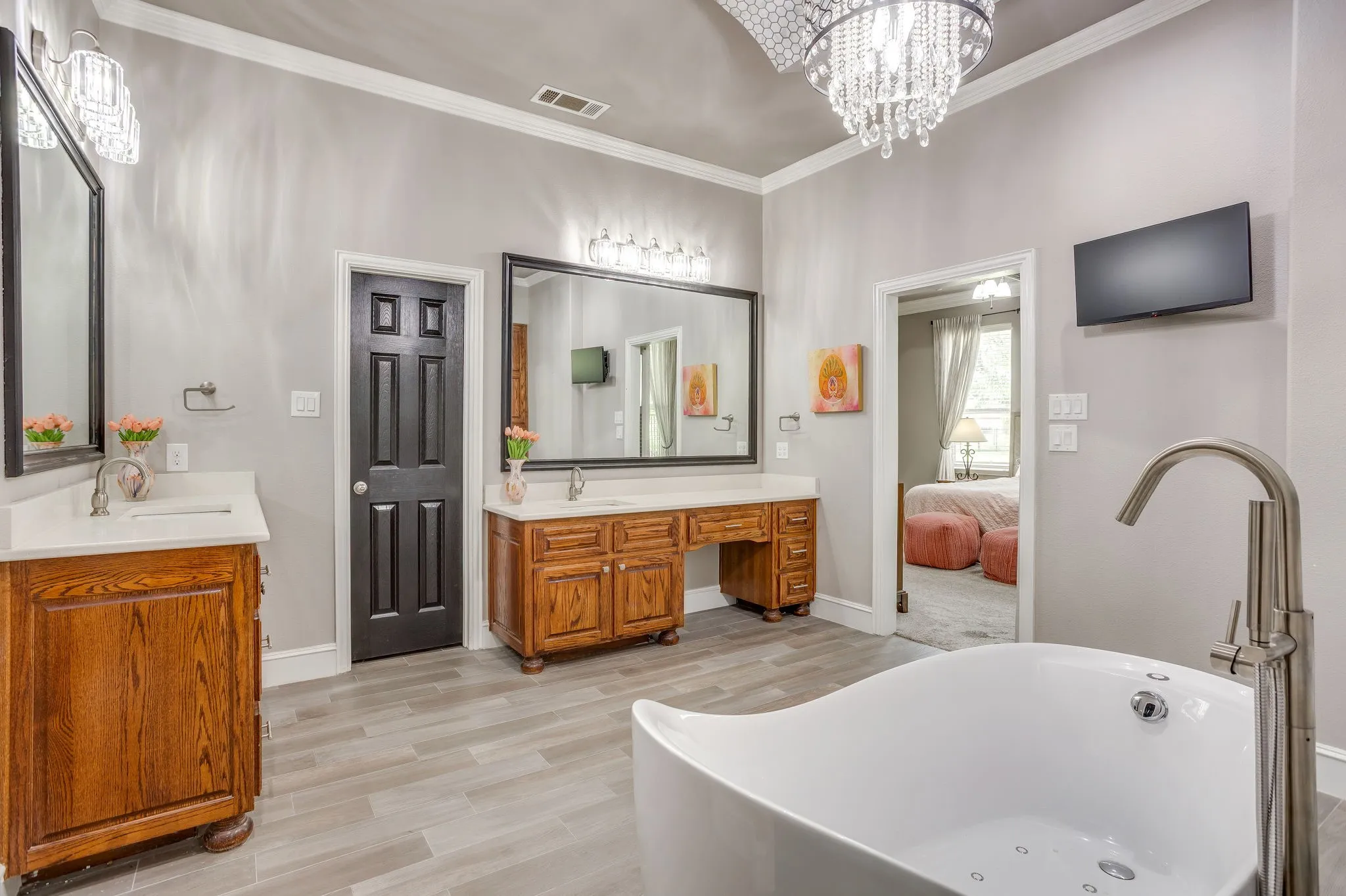 Freestanding soaking tub with a floor-mounted brushed nickel faucet, two wood-finish vanities with undermount sinks and quartz countertops, and a decorative ceiling chandelier