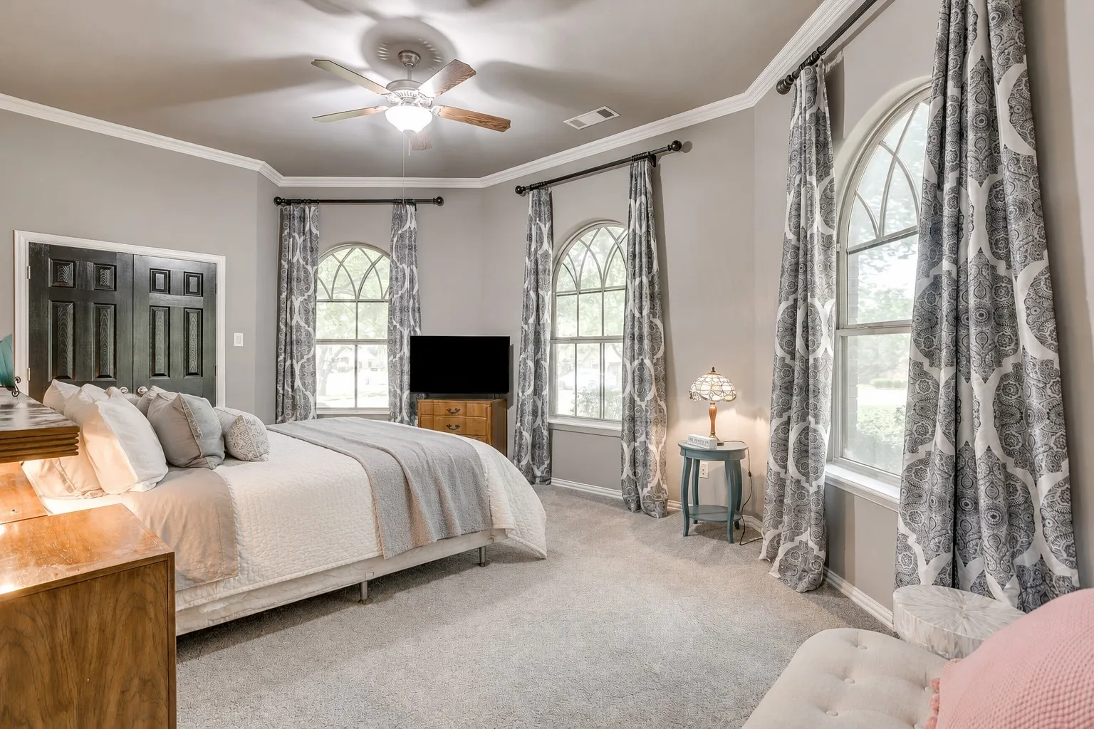 Spacious room featuring arched windows with decorative grilles, neutral carpet flooring, and a ceiling fan with integrated lighting