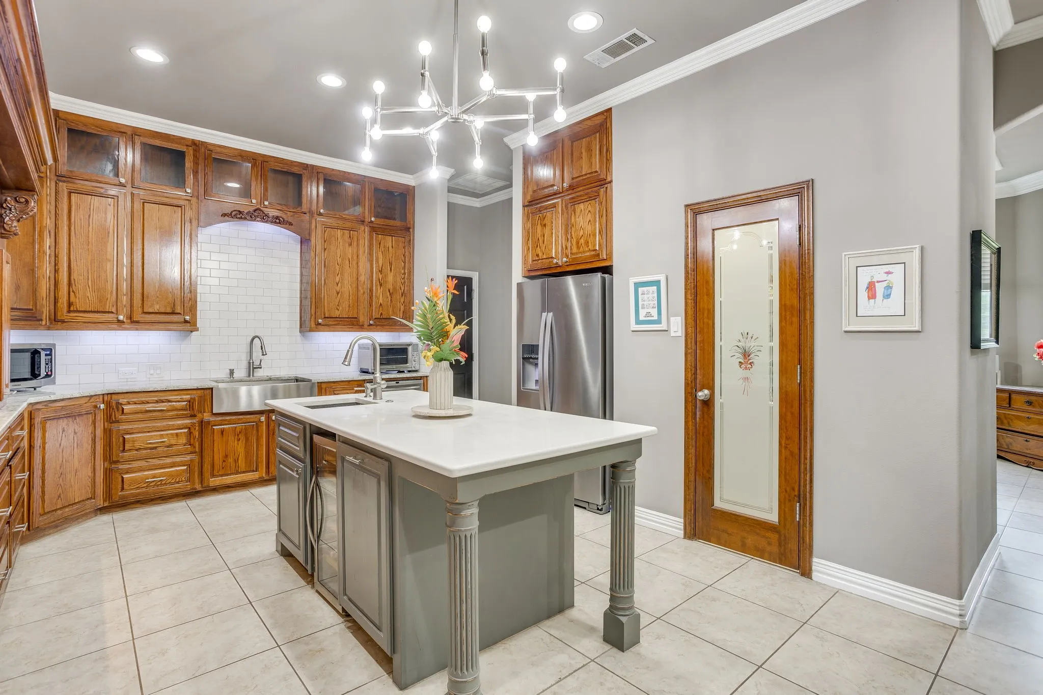 Spacious kitchen featuring a central island with a solid surface countertop, warm wood-finish cabinetry, subway tile backsplash, and a large stainless steel sink
