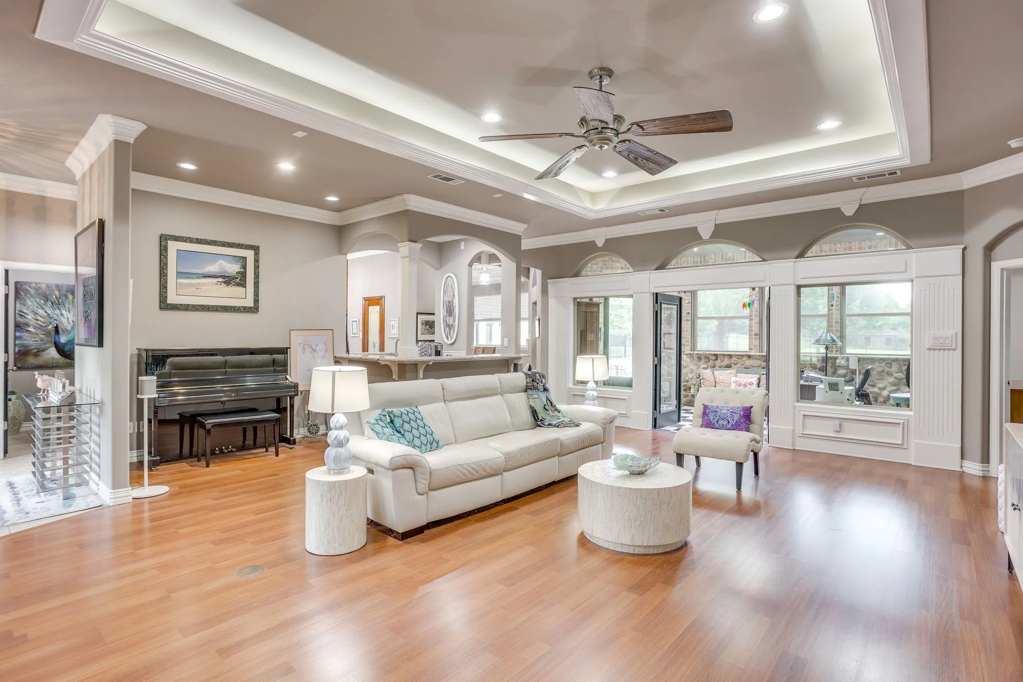 Spacious living area featuring wood-finish flooring, a tray ceiling with recessed lighting, and a ceiling fan