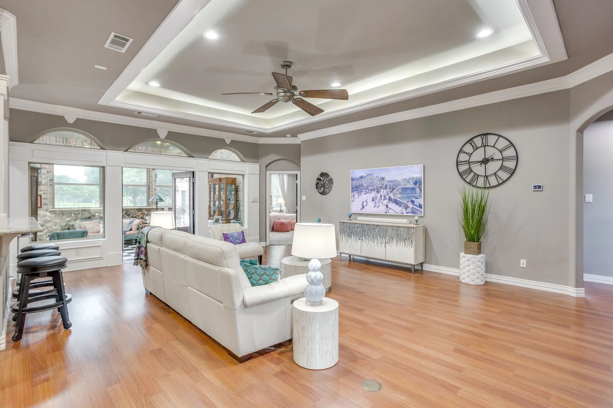 Spacious living area featuring wood-finish flooring, a tray ceiling with recessed lighting, and a ceiling fan