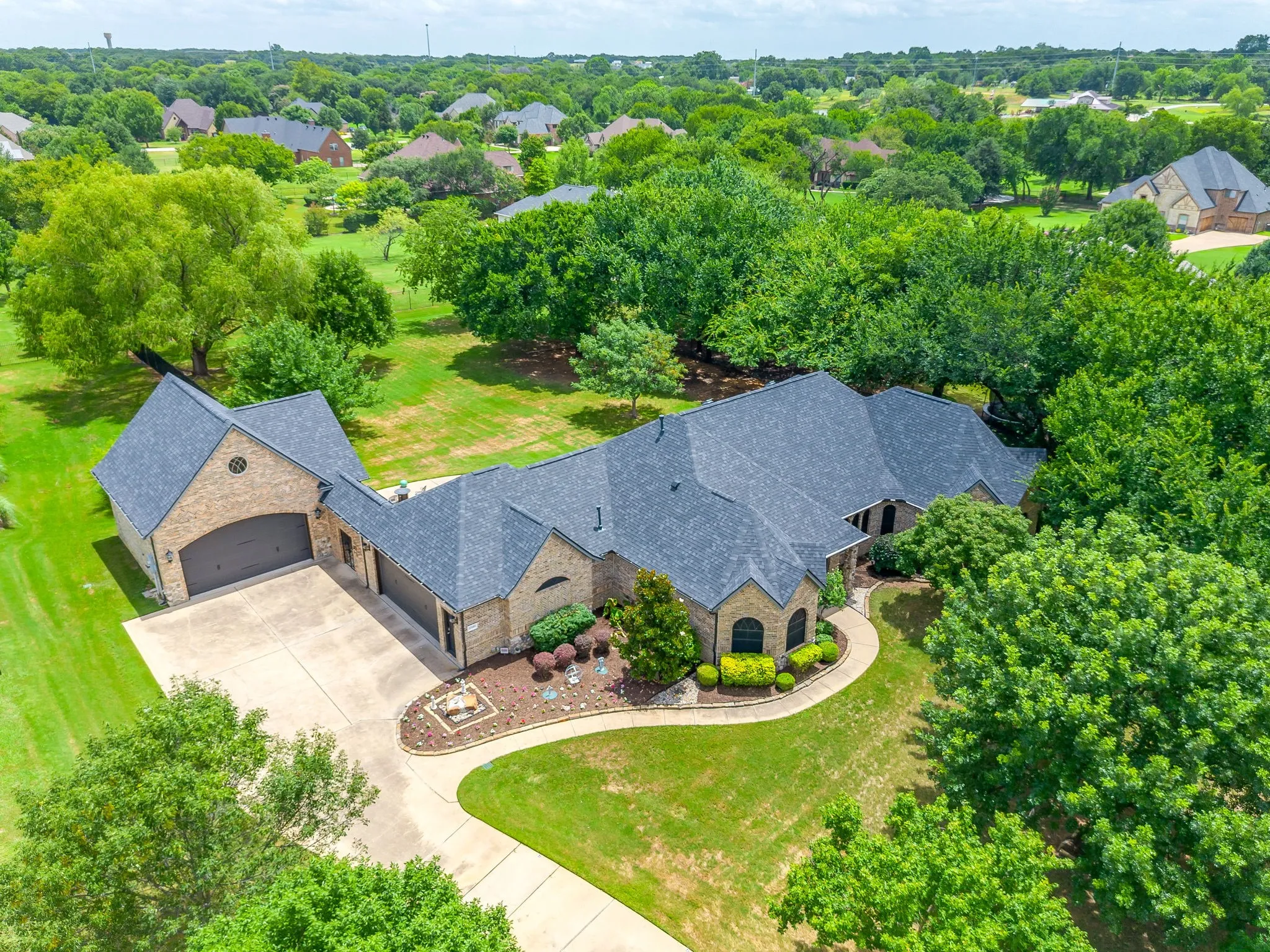Expansive brick exterior residence featuring a multi-car garage, mature landscaping, and a curvilinear driveway