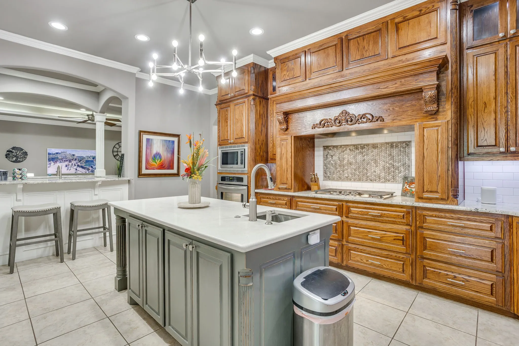 Kitchen featuring a large central island with a sink and light-toned countertop, extensive wood cabinetry, a tiled backsplash above the range, and recessed lighting