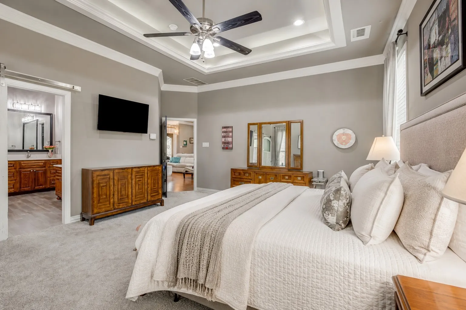 Carpeted bedroom featuring a tray ceiling with a ceiling fan, a wall-mounted television, and a barn door entry to the bathroom