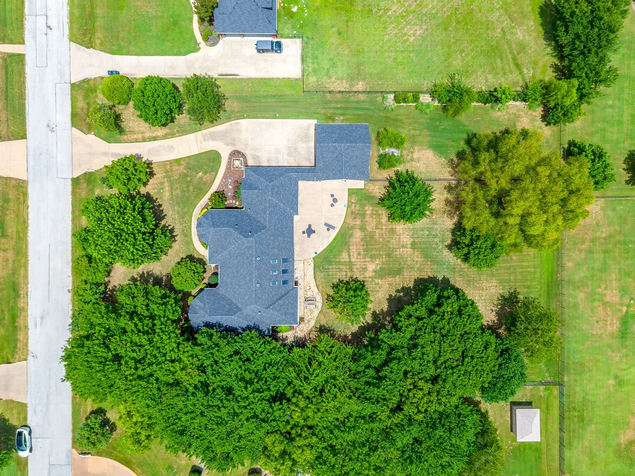 Aerial perspective showcasing a property with a dark shingle roof and extensive concrete paving