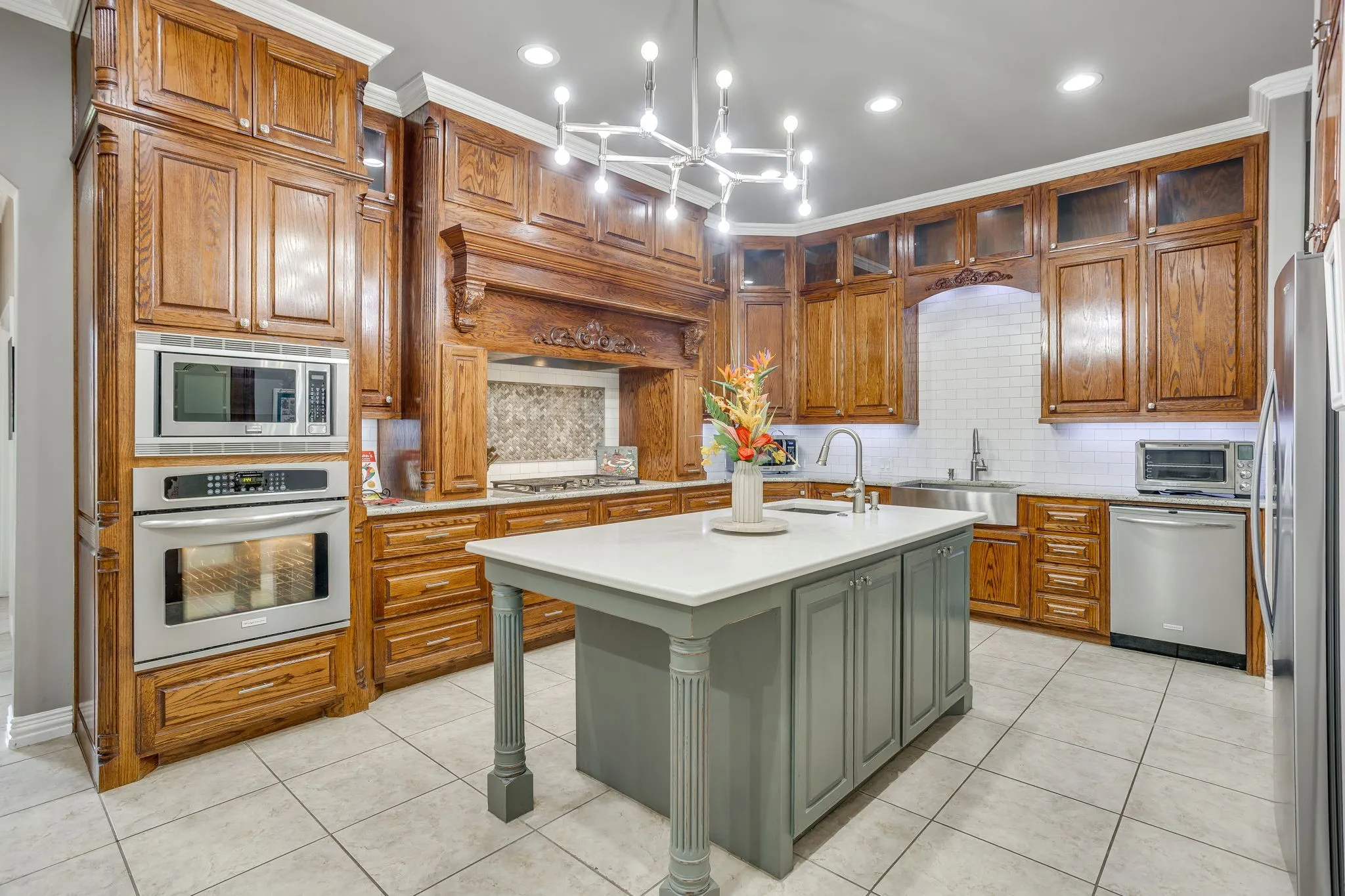 Kitchen featuring rich wood cabinetry, stainless steel appliances, a center island with a light-toned countertop, a tile backsplash, and a modern chandelier