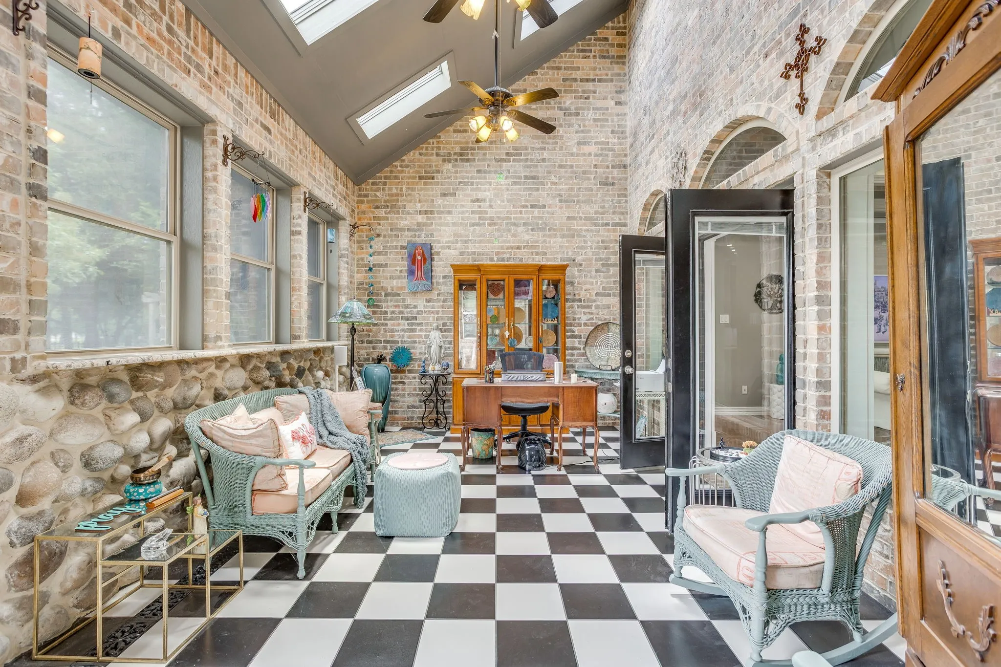 Sunroom featuring a vaulted ceiling with skylights, black and white checkerboard flooring, exposed brick walls, and a stone knee wall