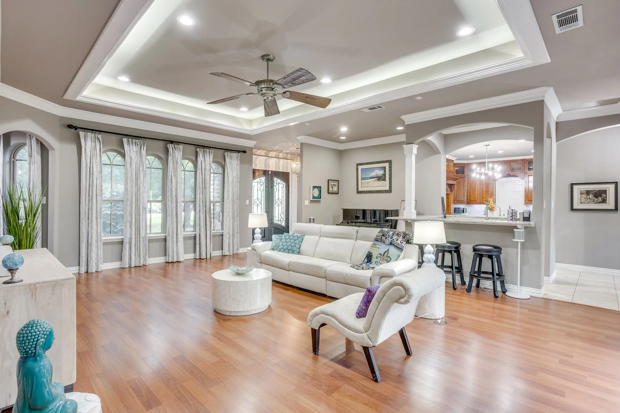 Spacious living area featuring wood-finish flooring, a tray ceiling with recessed lighting and a ceiling fan, and a series of arched windows