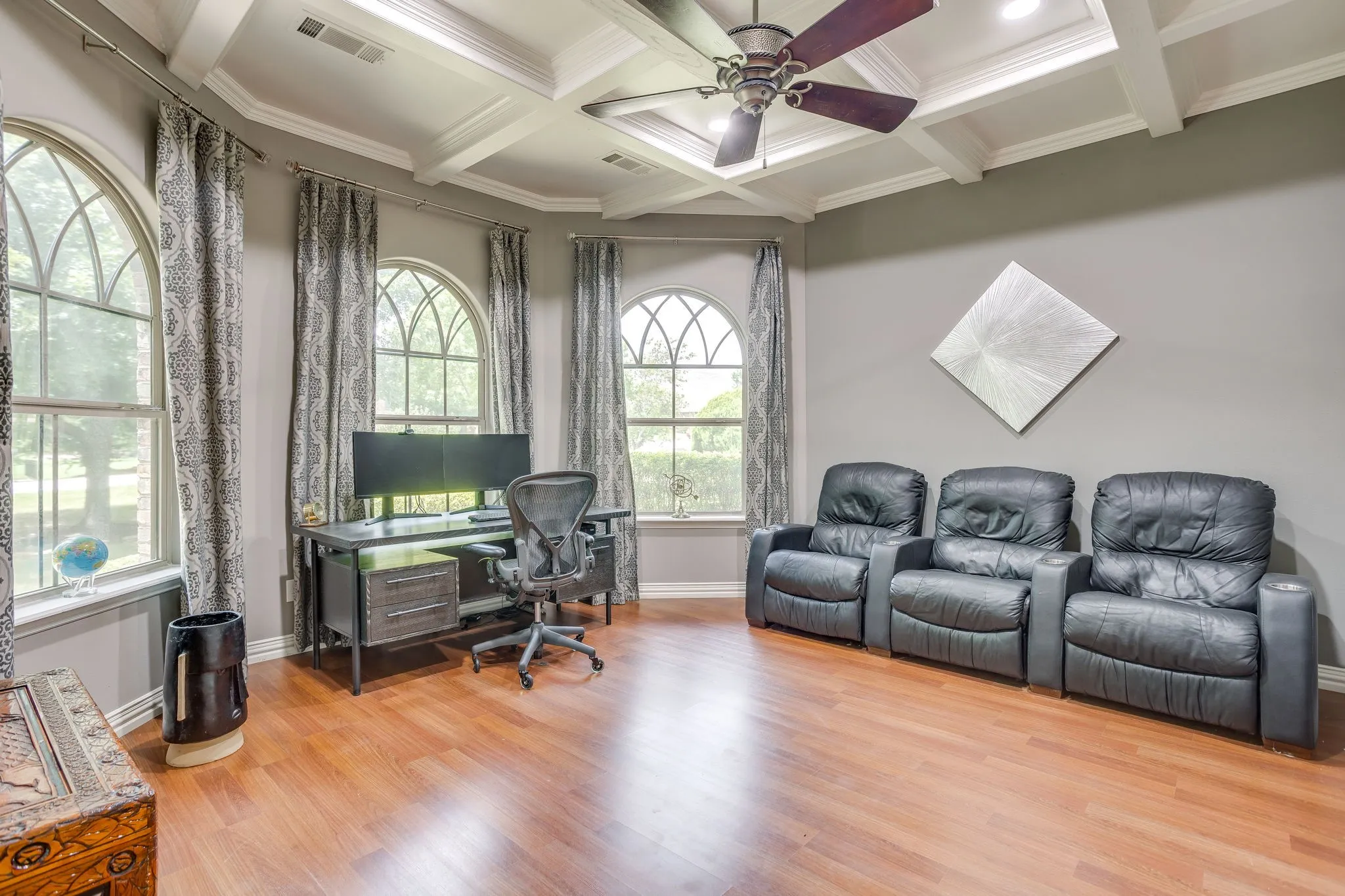 Room featuring arched windows, wood-finish flooring, and a coffered ceiling with a ceiling fan