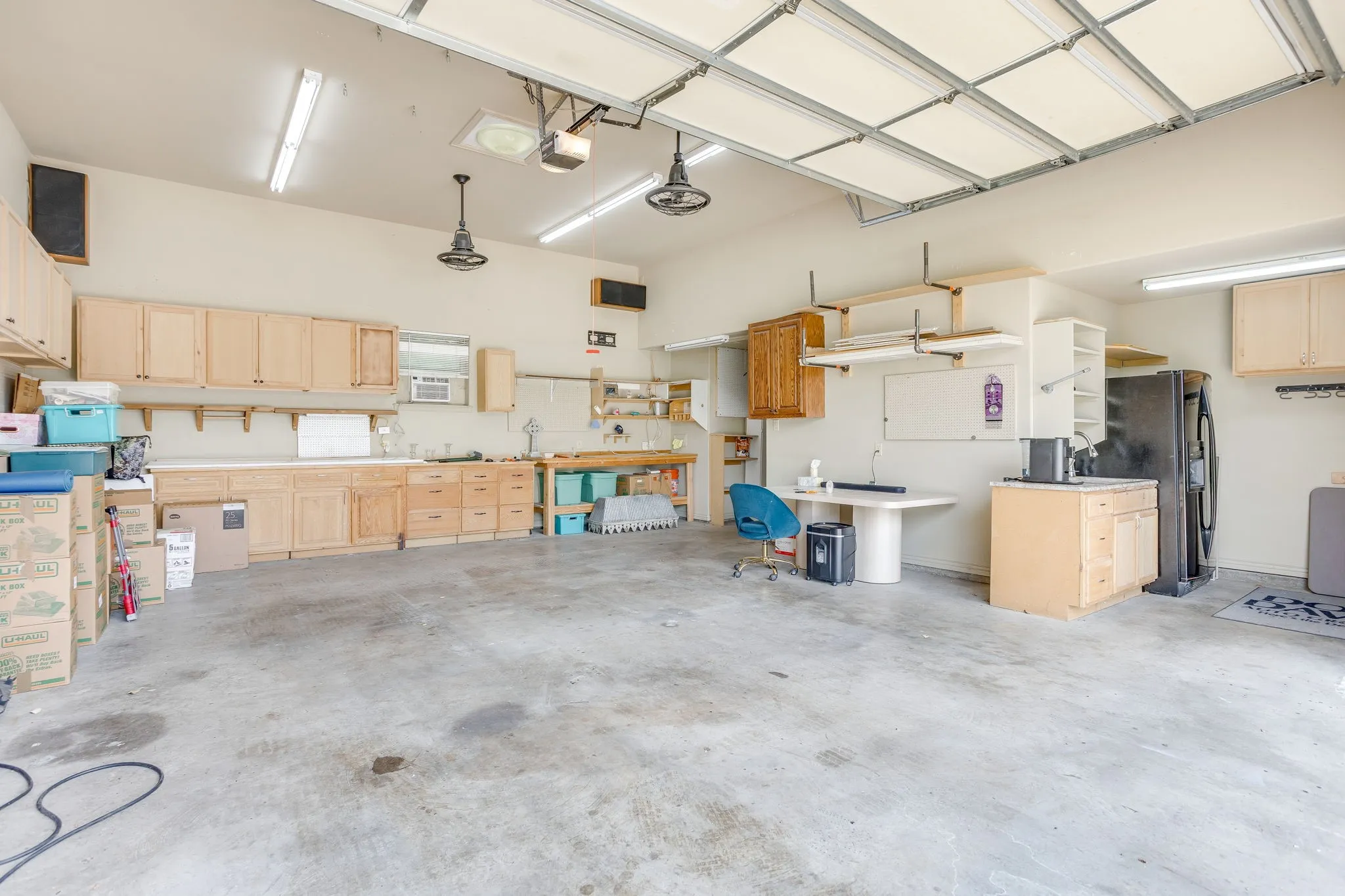 Spacious garage featuring extensive built-in cabinetry, concrete flooring, overhead fluorescent lighting, and industrial-style ceiling fans